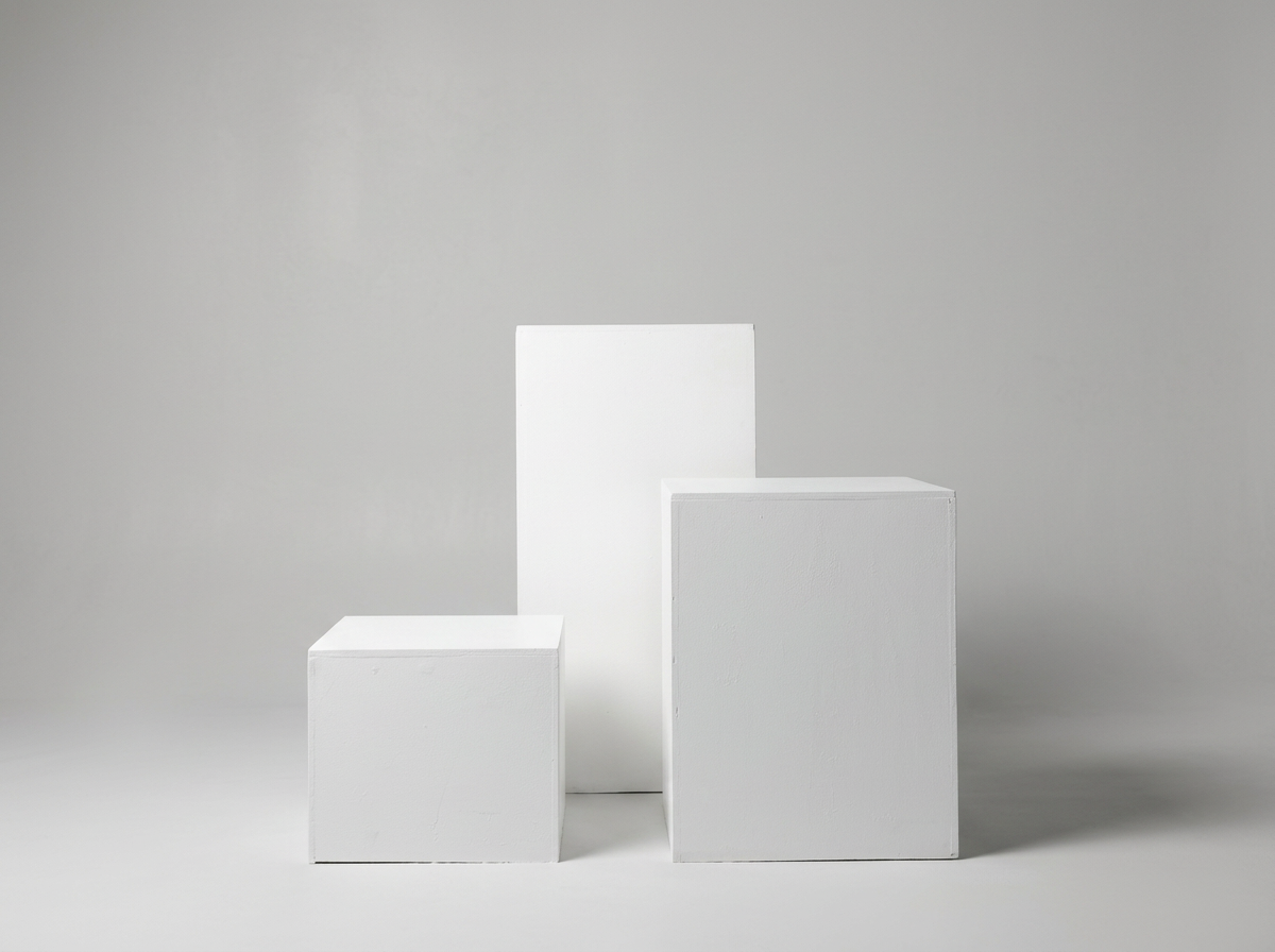 Three white display pedestals of varying heights on a plain gray background.