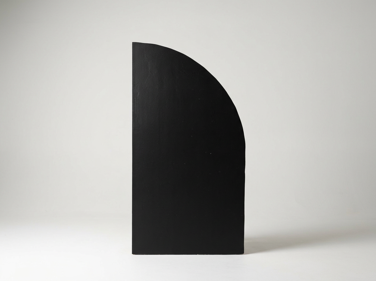 A black, semi-circular object standing upright on a white surface with a plain white background.