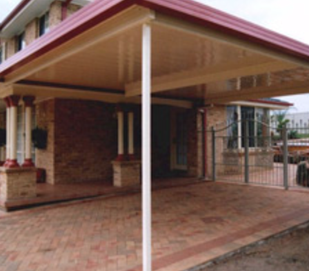 Covered patio area with brick flooring and supporting columns in front of a brick building.