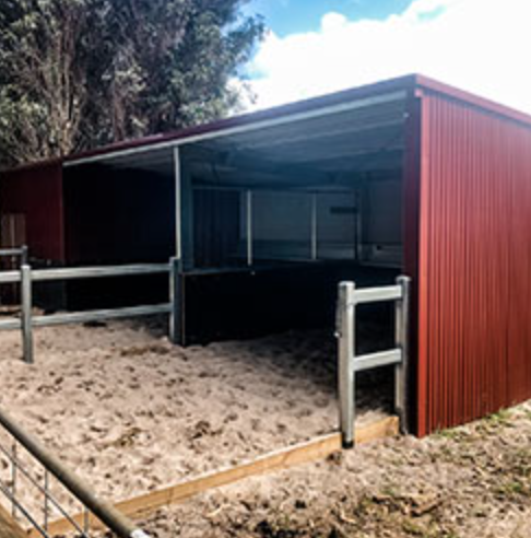 Empty open horse stable with a dirt floor and wooden fence.