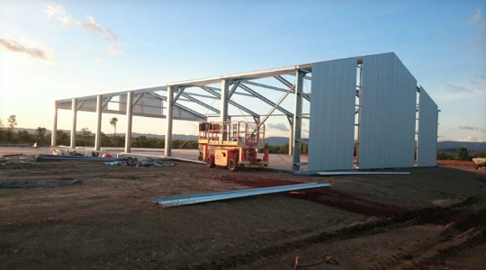 Construction site with a partially built metal warehouse and a crane in the foreground.