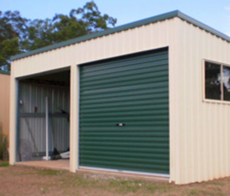 A metal storage shed with a green rolling door and a window, situated outdoors on a grassy area.