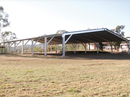 Empty metal carport with a slanted roof on a grassy field.
