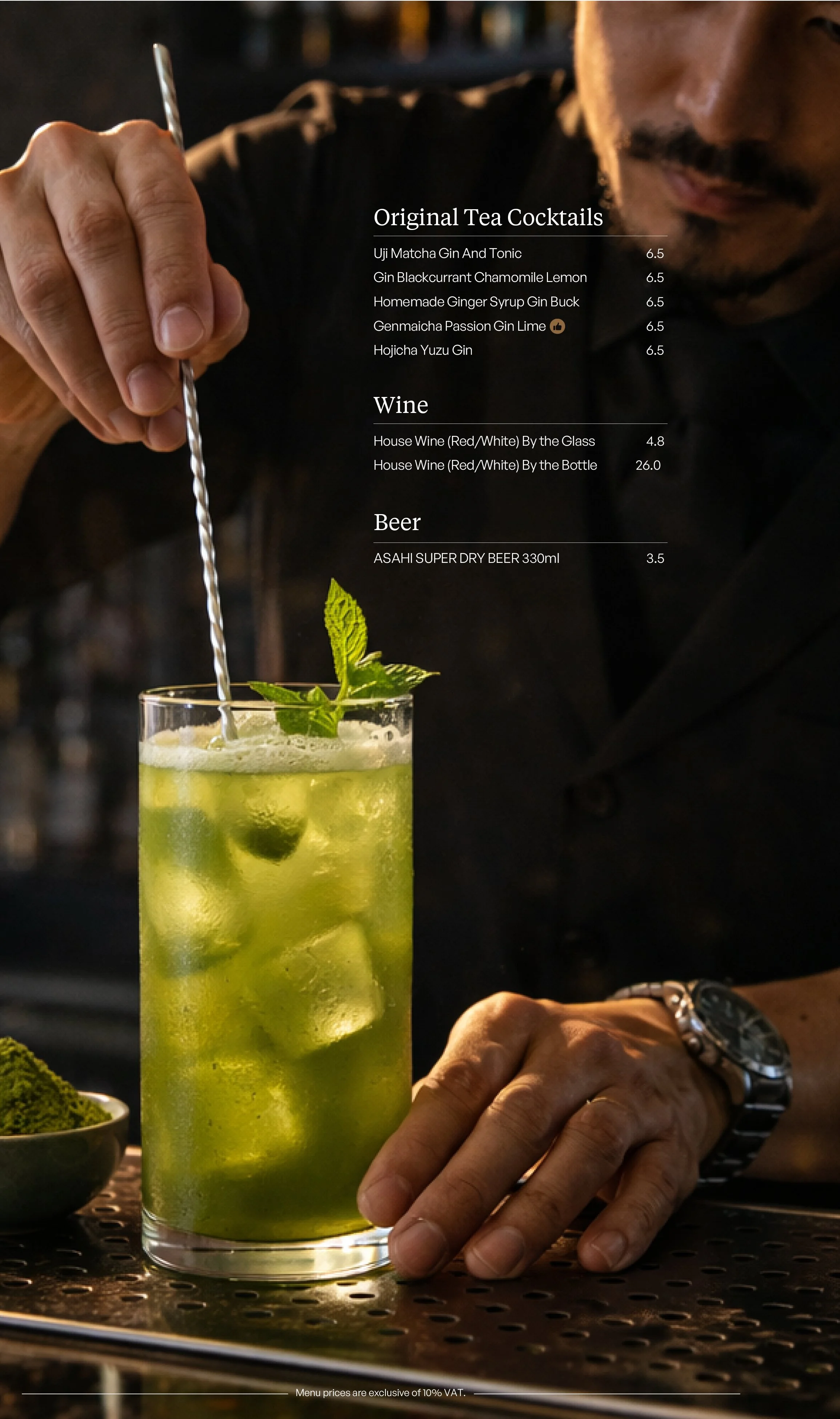 A person holding a tall glass of green cocktail with mint leaves and ice cubes, garnished with a mint sprig, and a bar menu in the background listing tea cocktails, wine, and beer options.