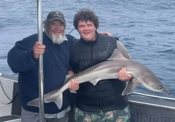 Two men on a boat holding a large fish they caught together, smiling at the camera.
