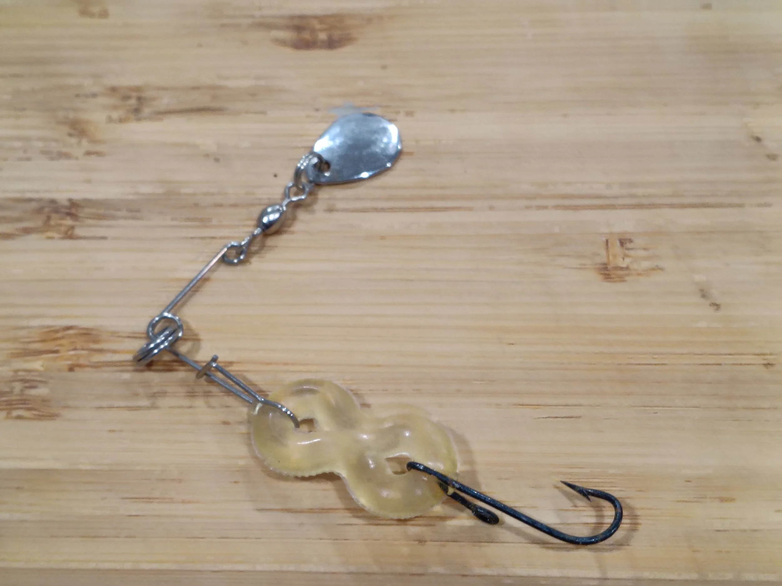 A fishing lure with a shiny metallic spoon attached to a chain, lying on a wooden surface.