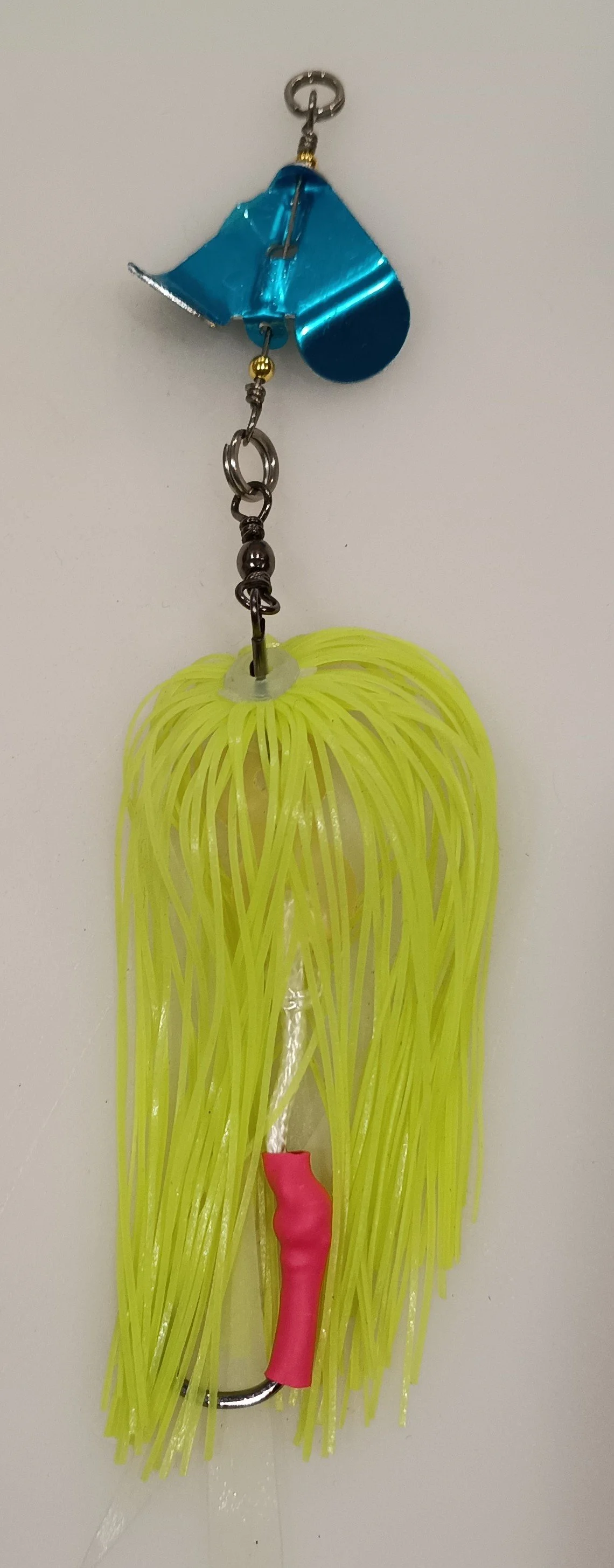 A fishing lure with a yellow skirt, pink hook cover, and blue metal blade, hanging from a metal keychain.