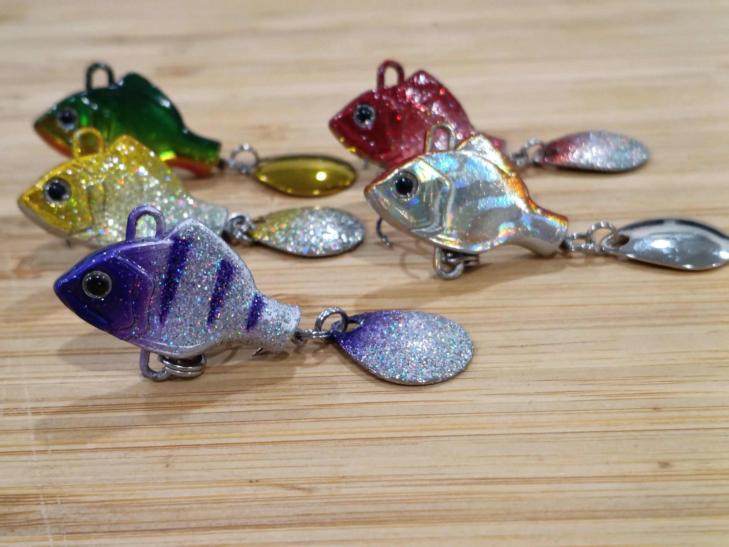 Colorful fishing lures shaped like fish with glitter, arranged on a wooden surface.