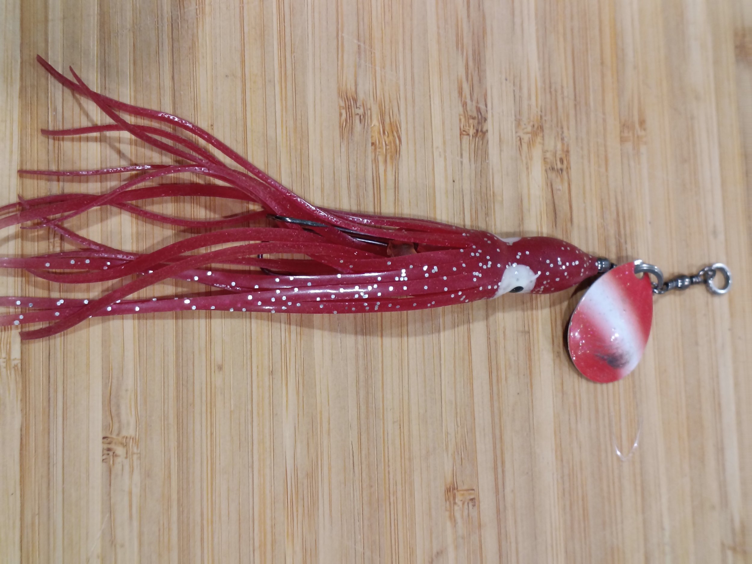 Red and white fishing lure with multiple tentacle-like appendages on a wooden surface.