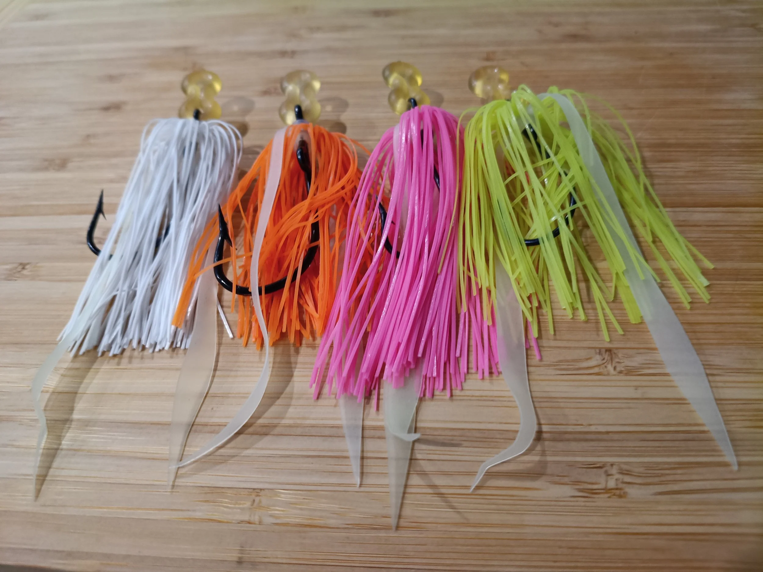 Four soft plastic fishing lures with various colors and hooks, laying on a wooden surface.
