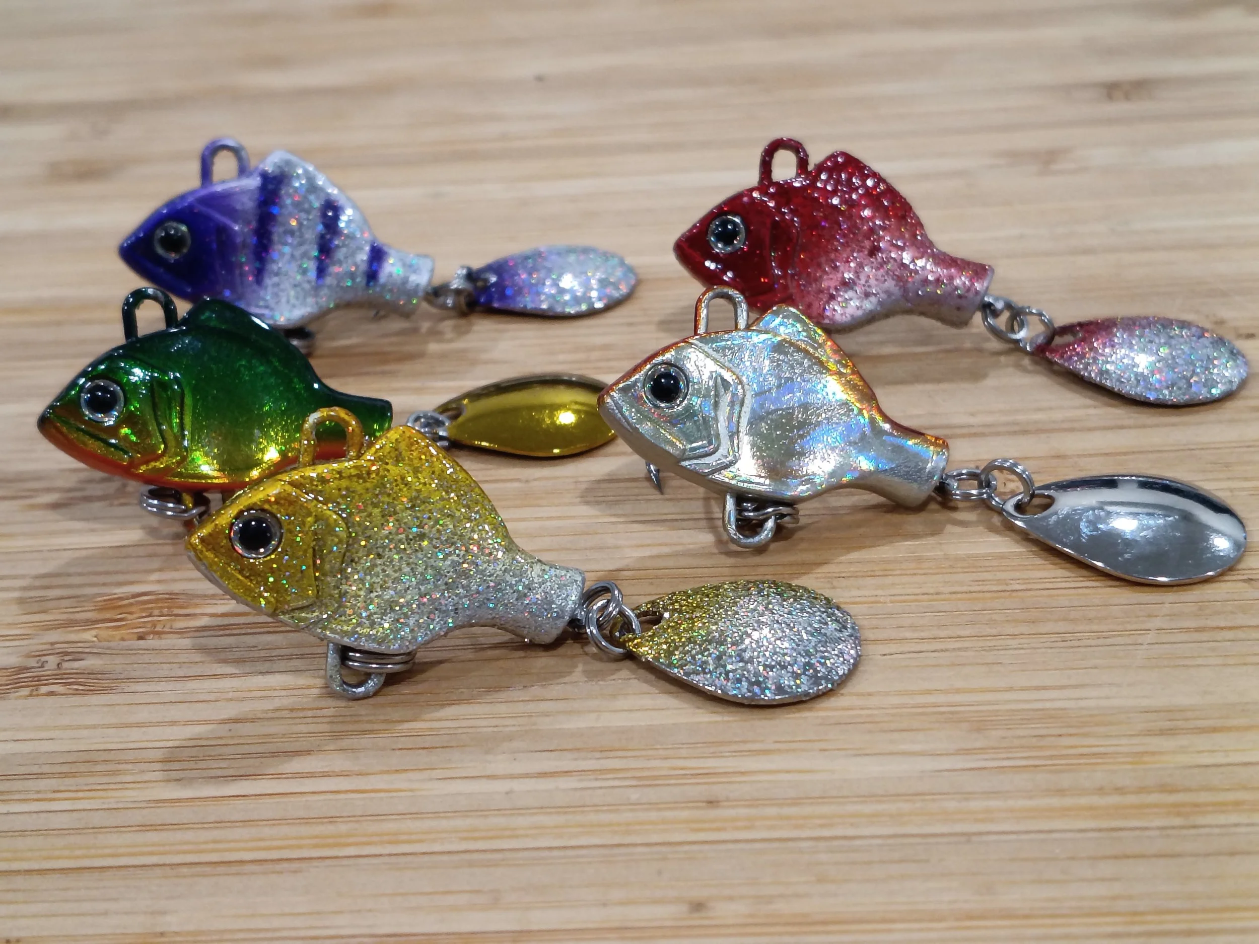 Colorful fish-shaped fishing lures with glitter on a wooden surface.