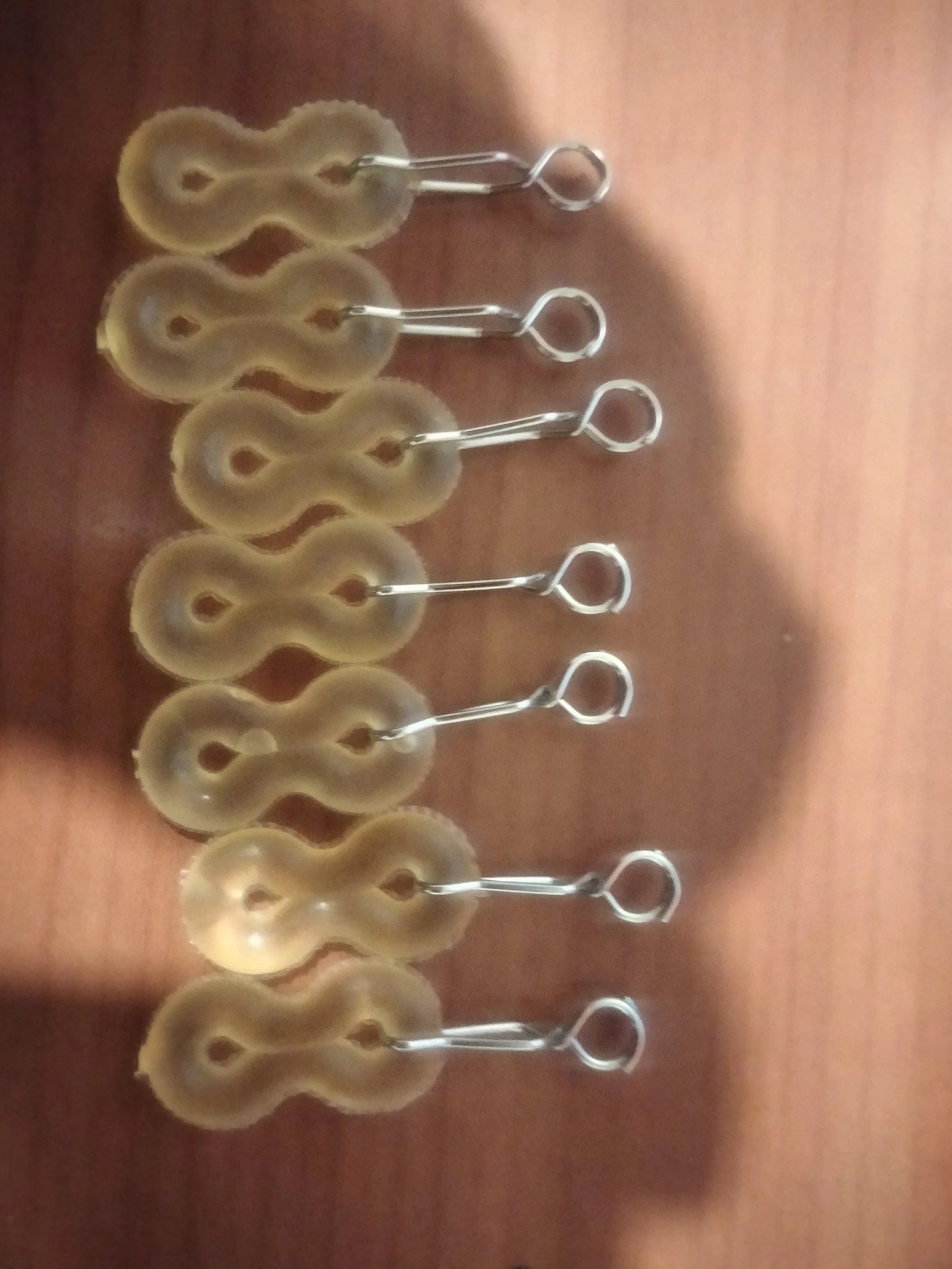A row of four decorative bathroom hooks with a metal loop at the top and beige and brown ceramic discus shaped bases, mounted on a wooden surface.