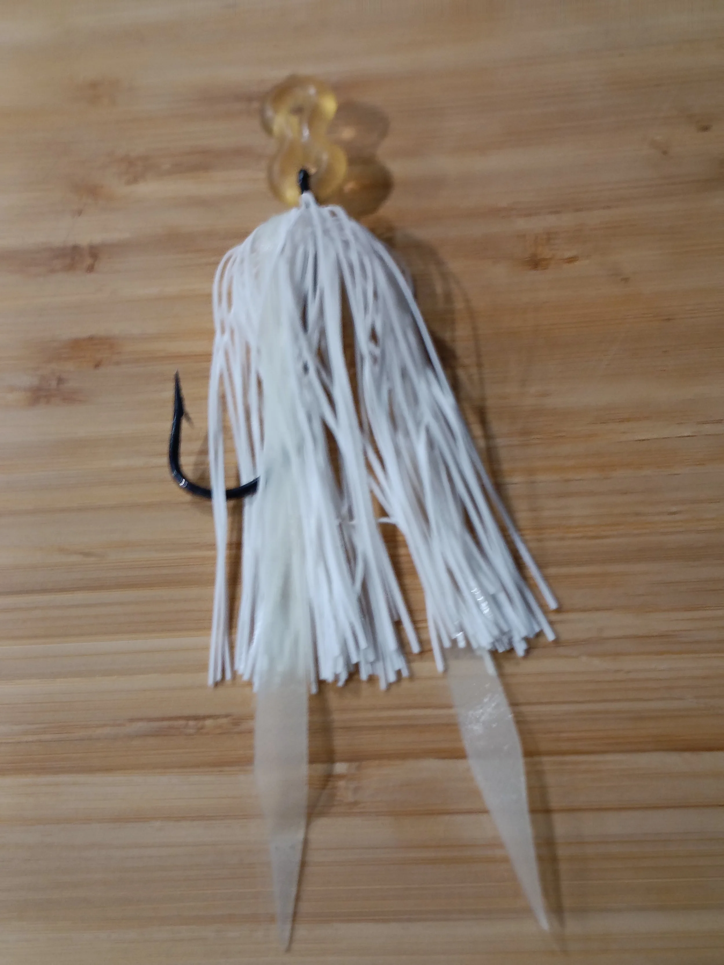 Close-up of a fishing lure with white strands and a black hook attached, lying on a wooden surface.