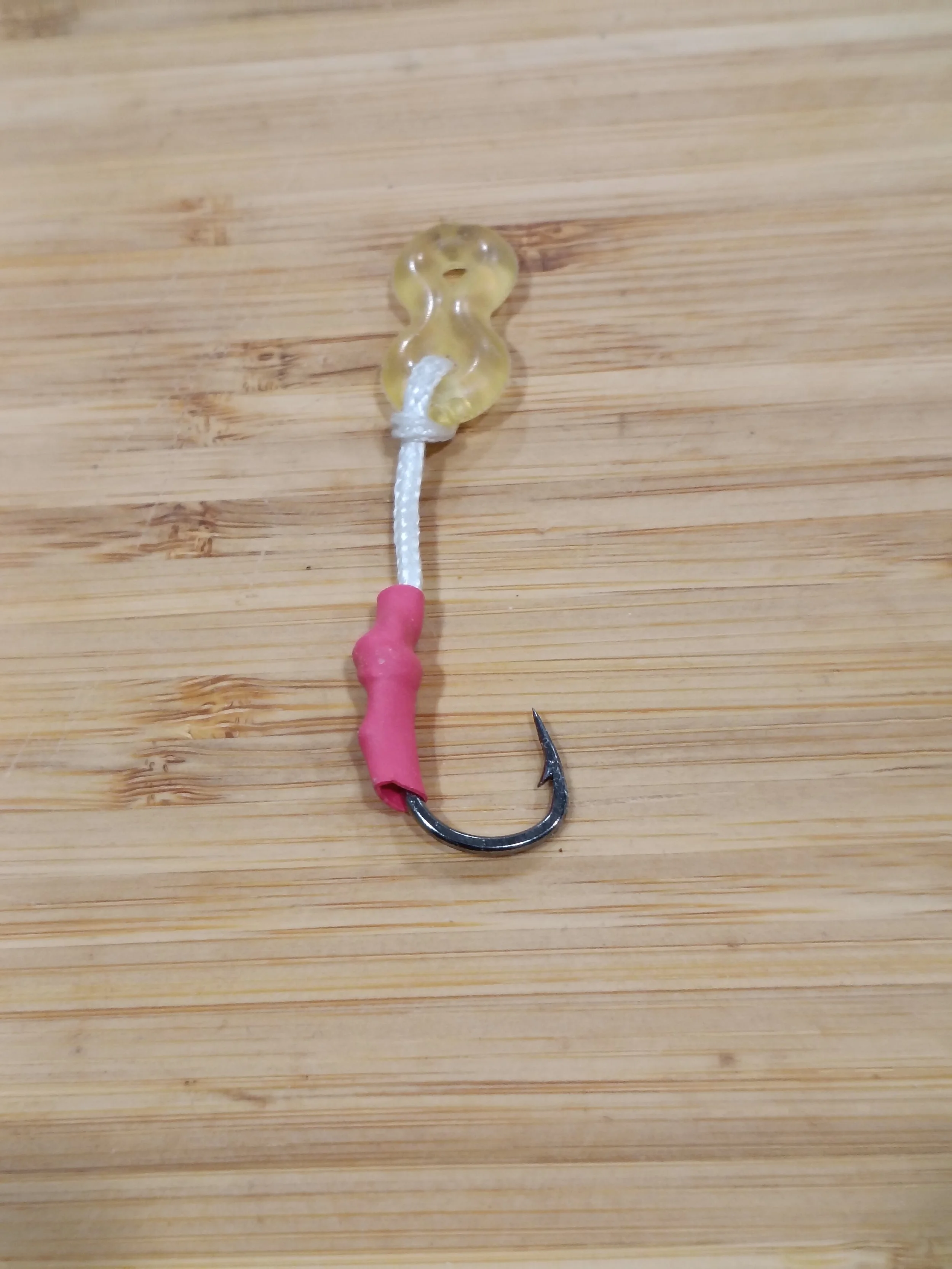 Close-up of a fishing hook with a soft plastic lure attached, lying on a wooden surface.