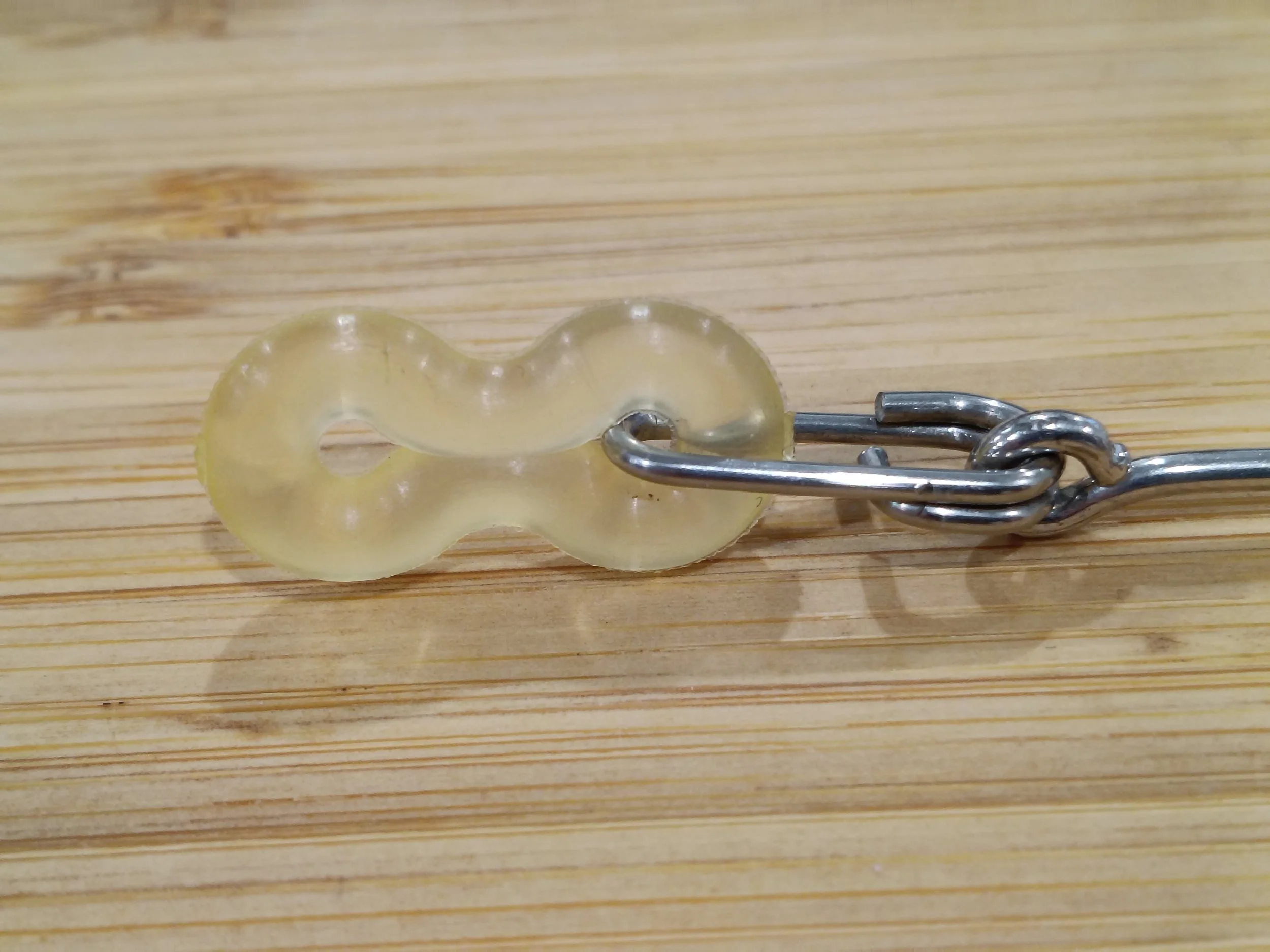 A plastic baby bottle with a metal chain attached, lying on a wooden surface.