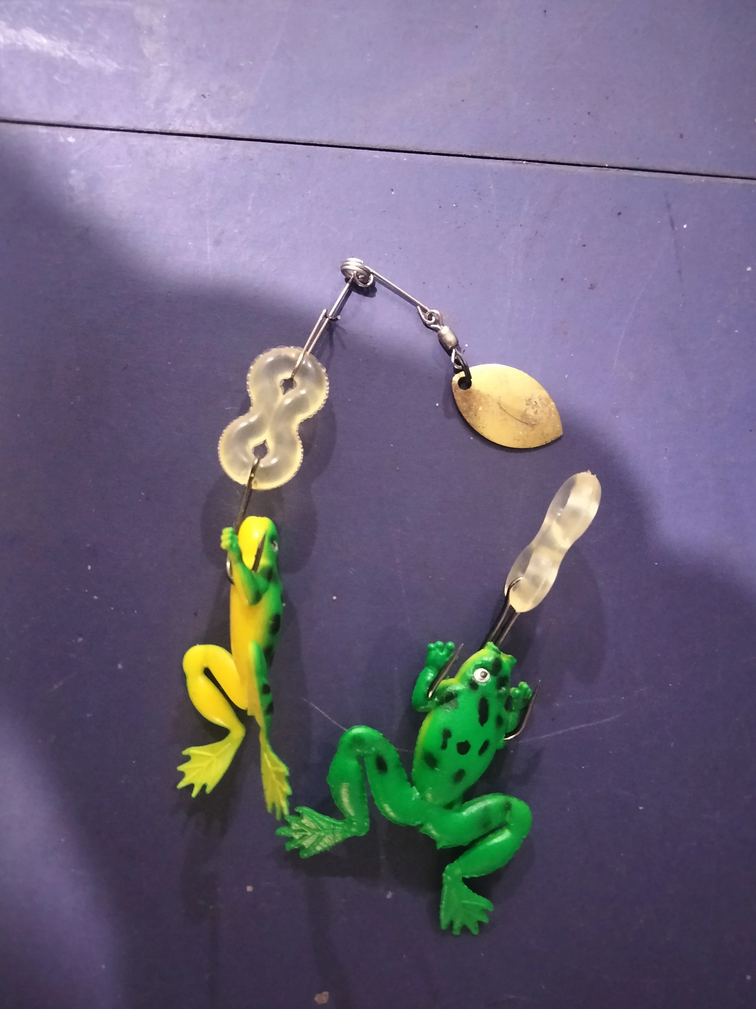 Collection of fishing lures shaped like frogs, frogs are yellow and green with black spots, displayed on a dark surface.