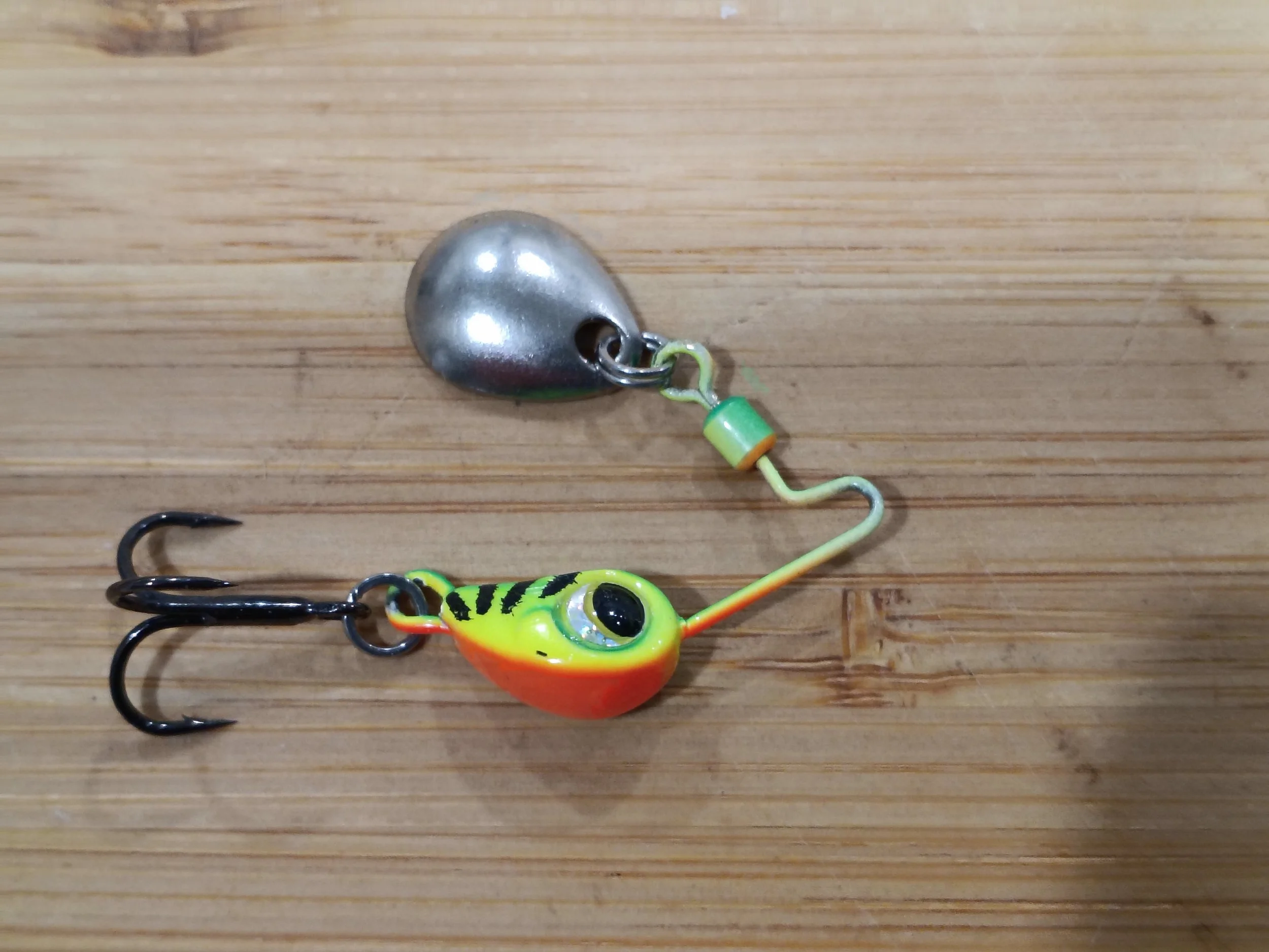 Colorful fishing lure with a frog design and a shiny metal weight attached, lying on a wooden surface.
