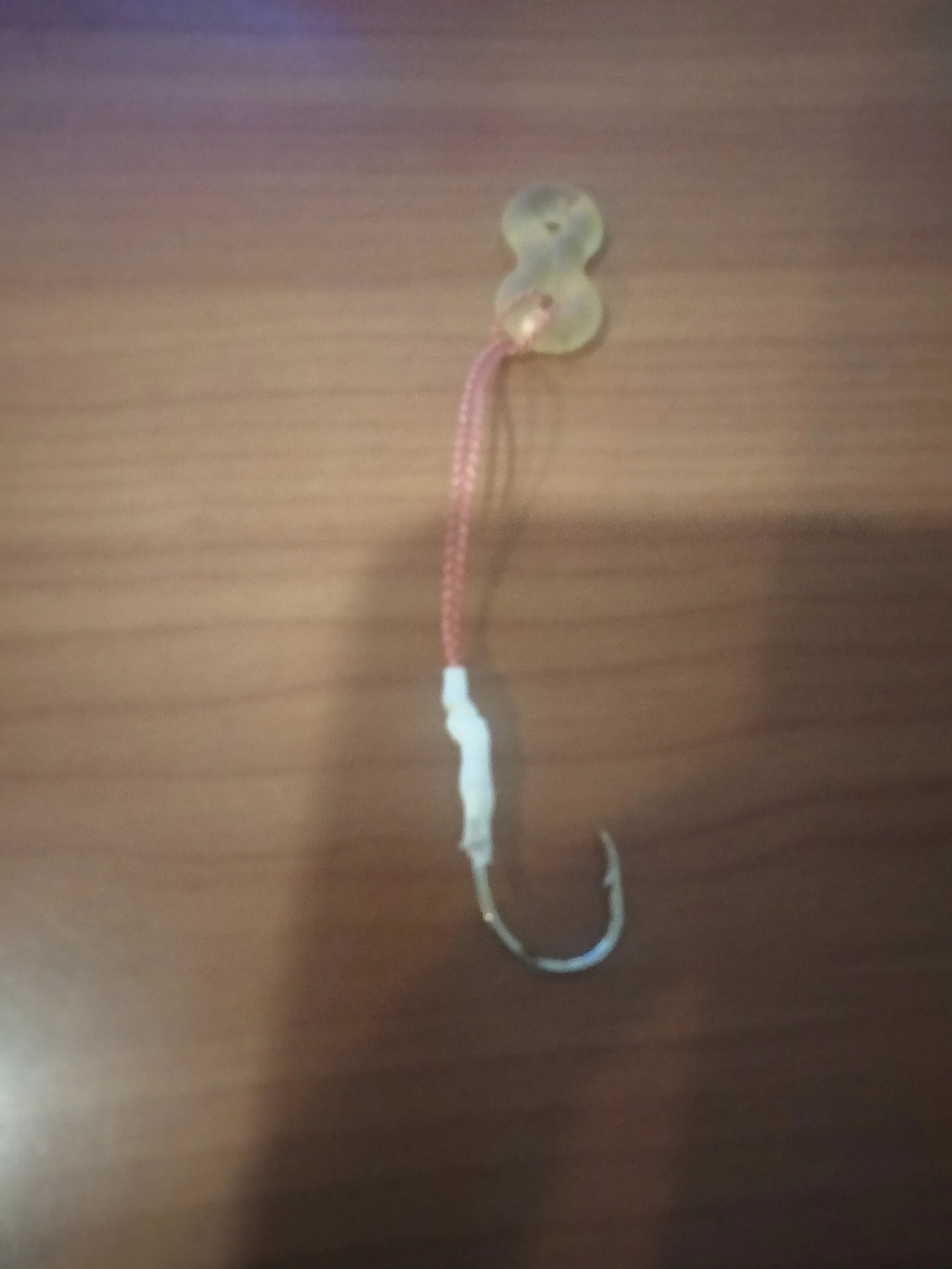 Close-up of a transparent plastic bait hook with a pink and white fishing lure attached, on a wooden surface.