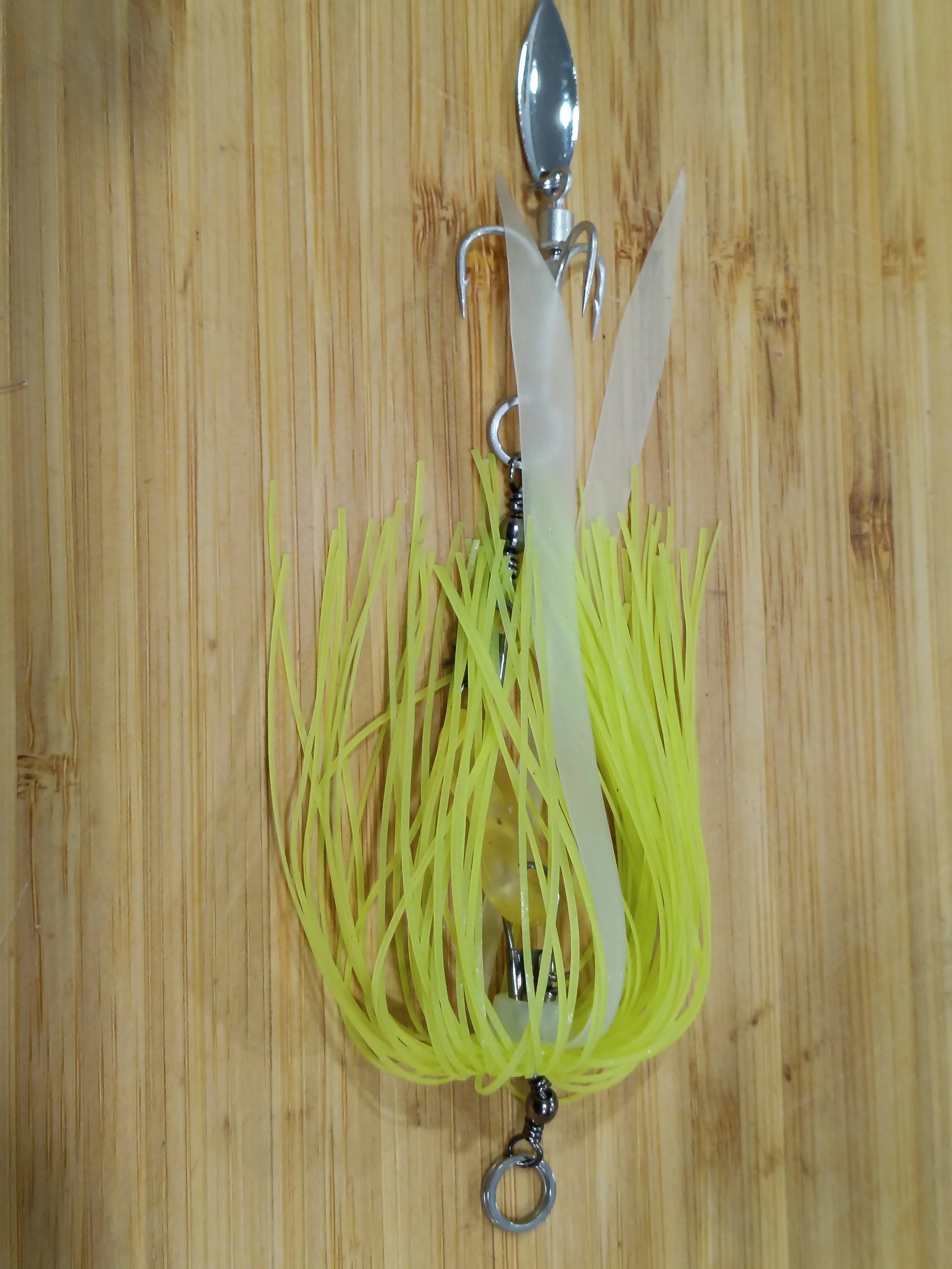 A decorative keychain with a yellow rubber band and small metal charms, featuring a fork and a knife, hanging against a wooden background.