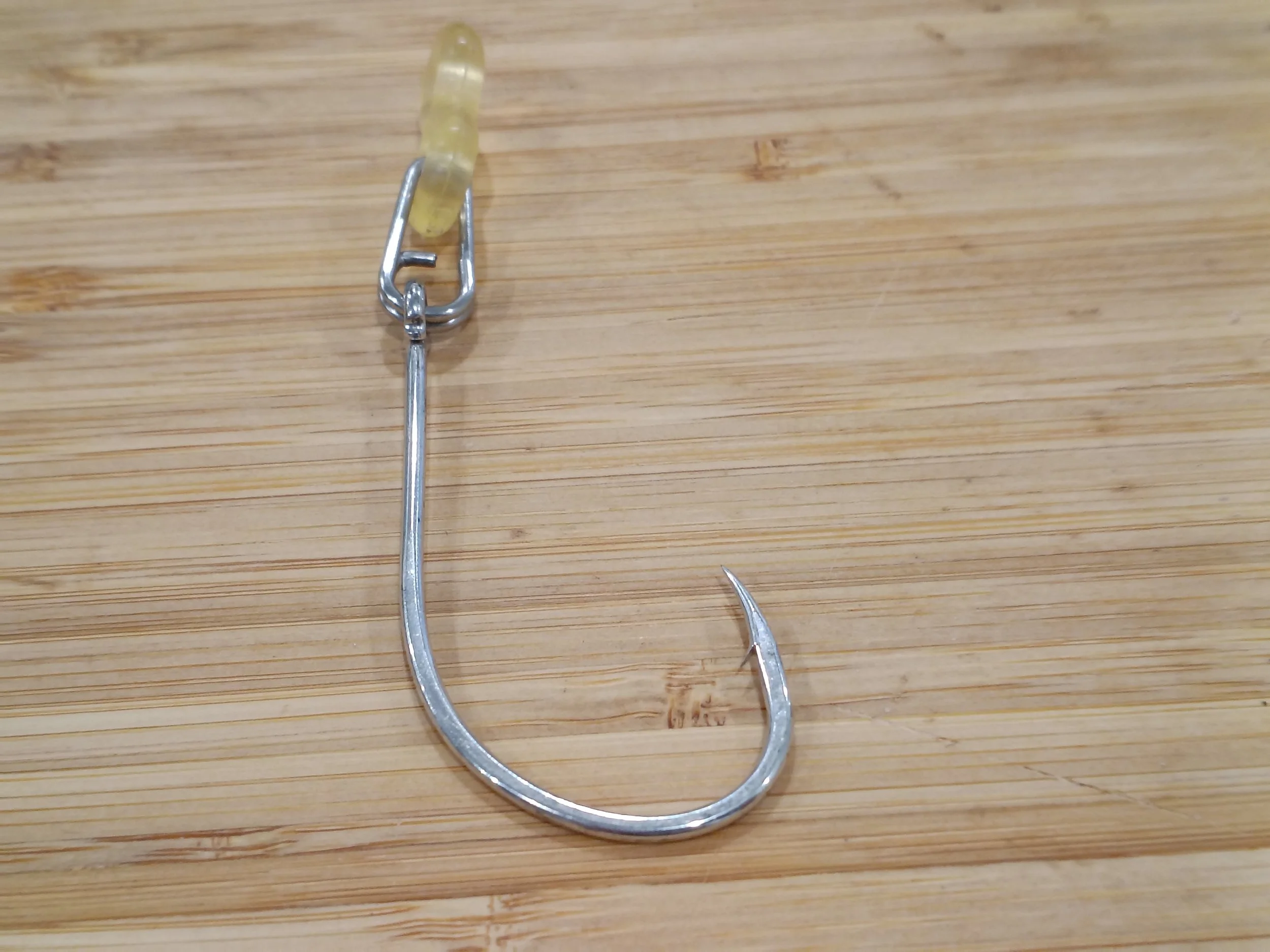 A metal fish hook on a wooden surface with a piece of bait attached.