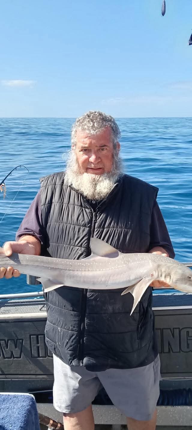 A man with gray hair and a beard holding a large fish on a boat at sea.
