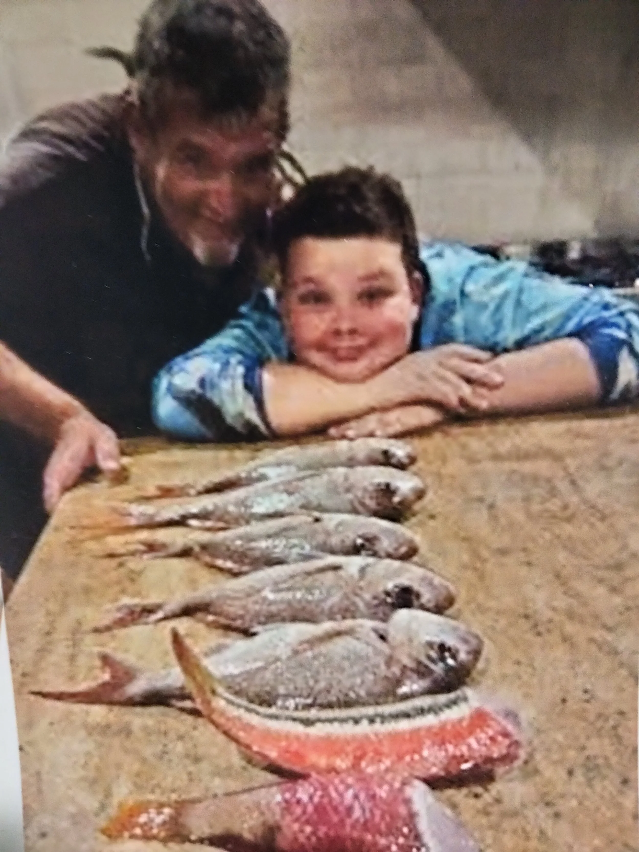 A young boy lying on the floor with a wide smile, surrounded by a line of small fish laid out in front of him.