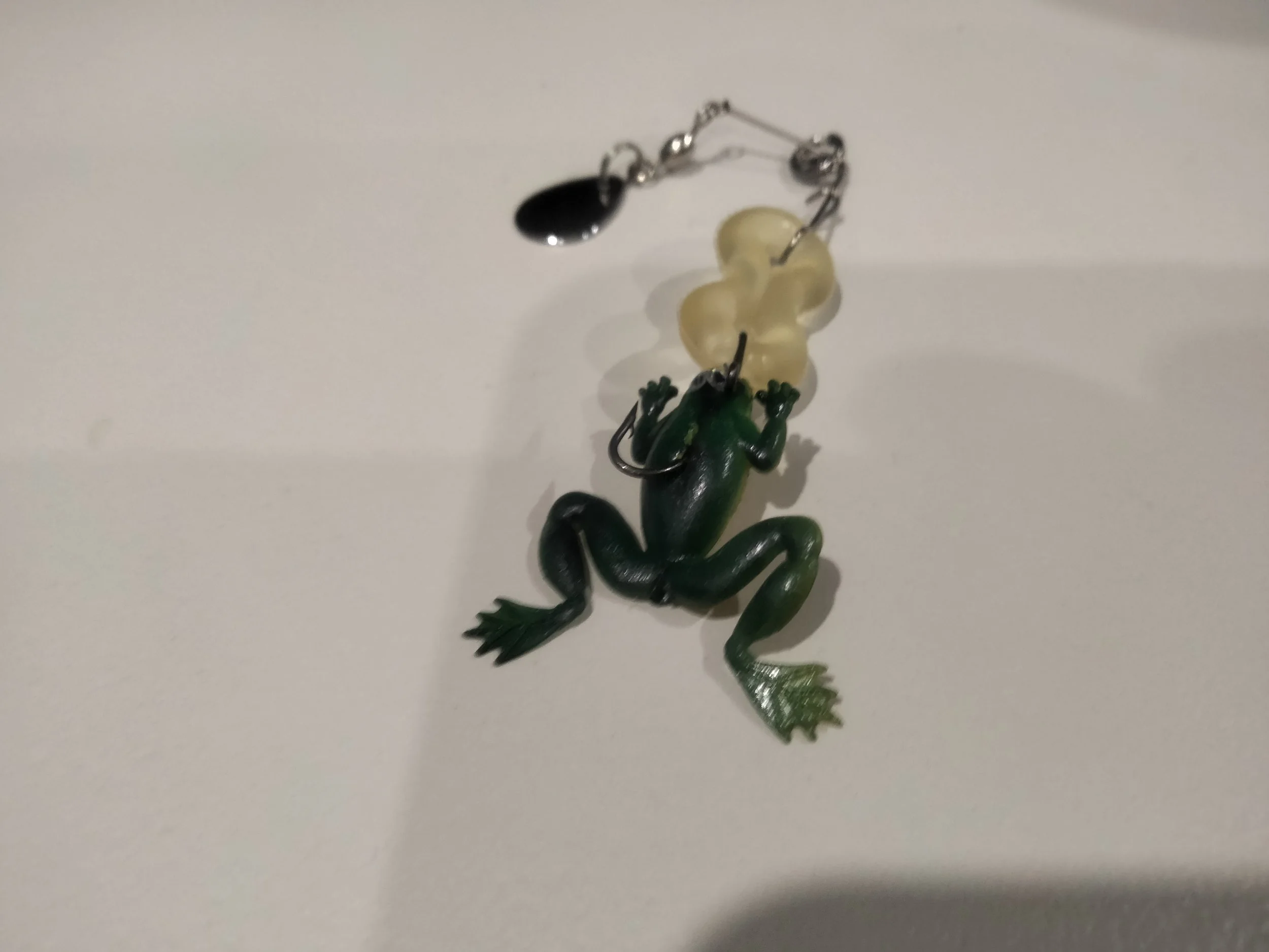Colorful fishing lure with green body, yellow head, black eyes, and silver hooks, placed on a white surface.