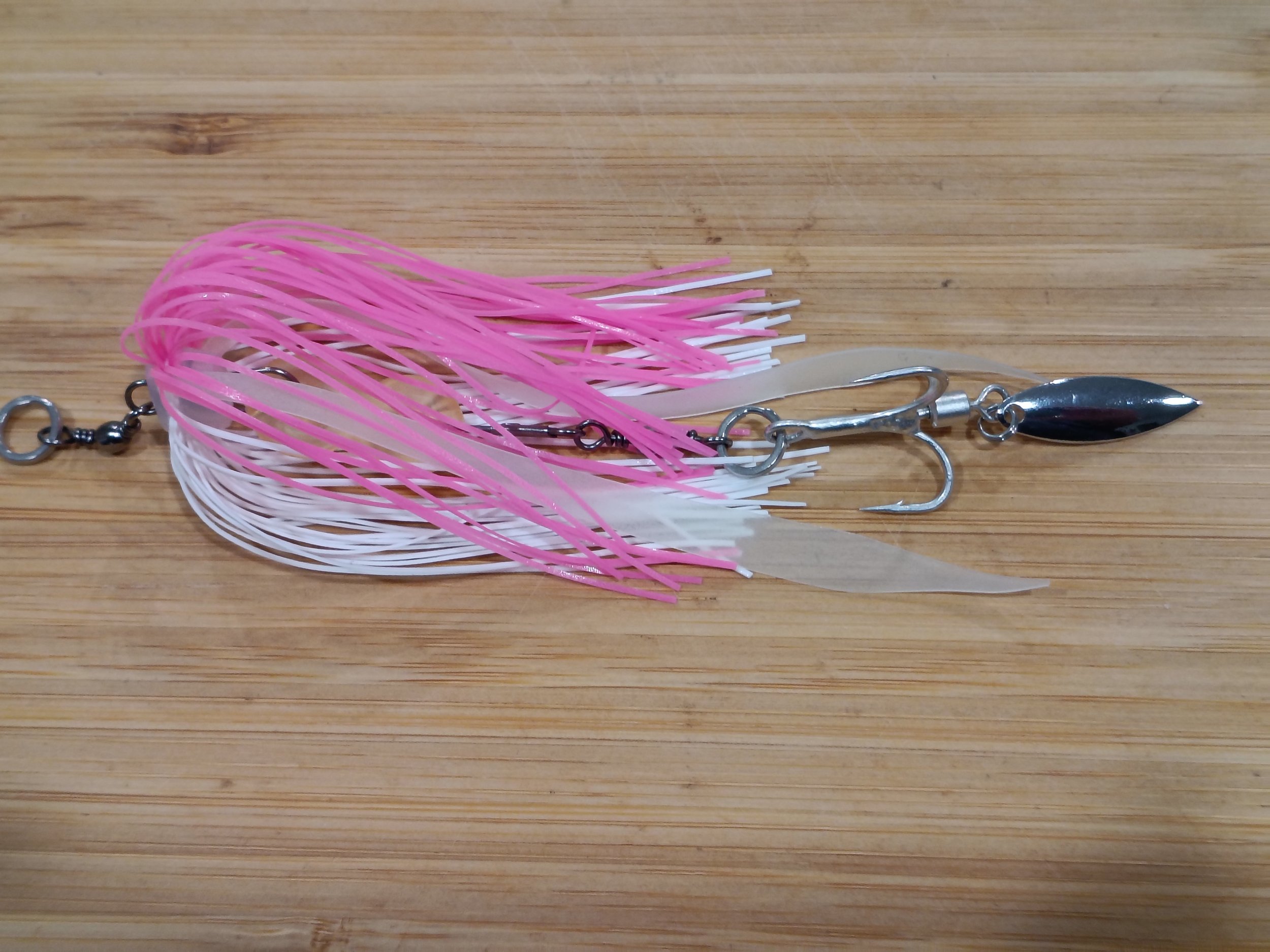Pink and white plastic baitfish lure with metal hooks and a spinner blade on a wooden surface.