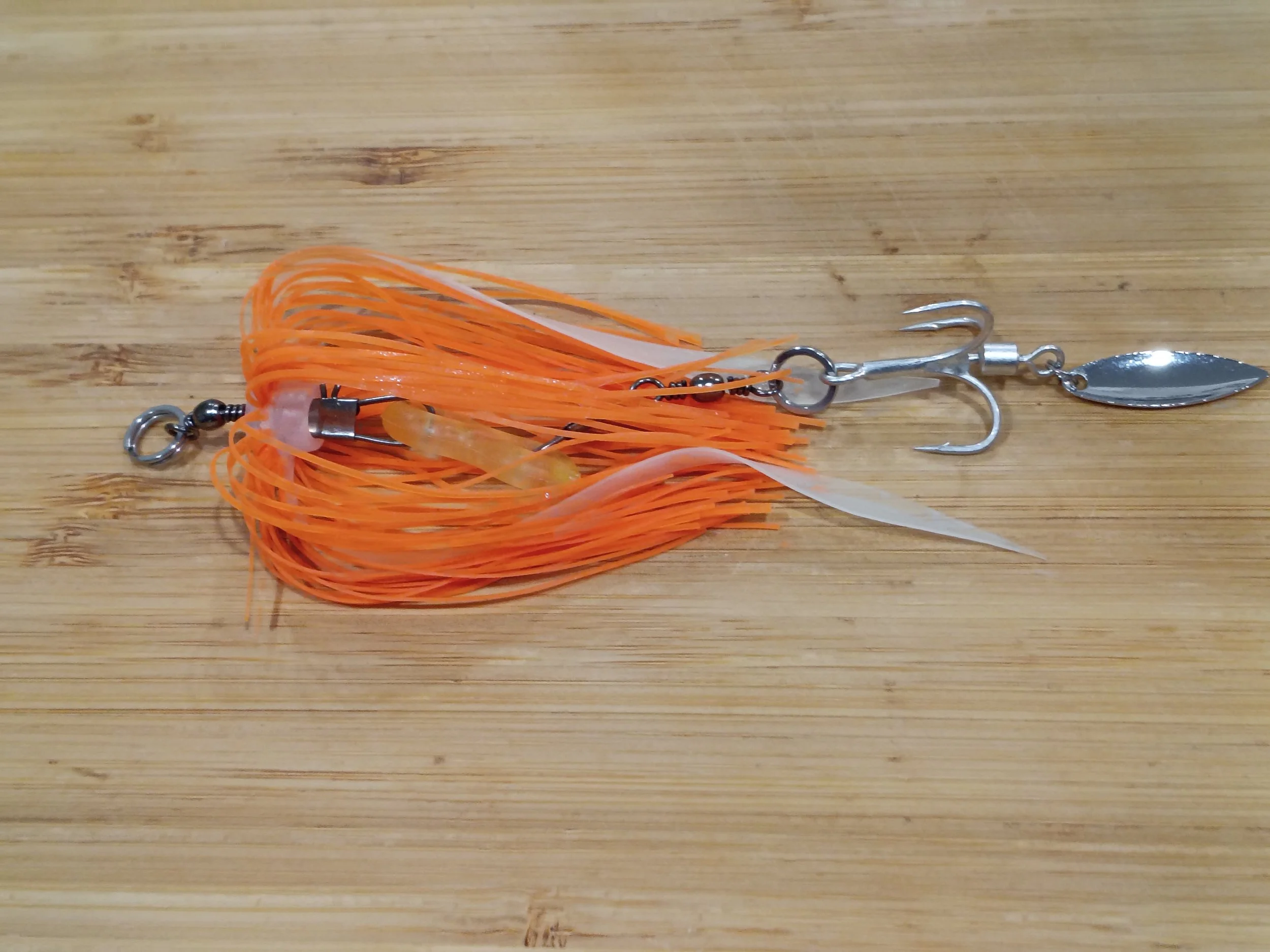 A fishing lure with orange and white rubber strands and a metal hook, lying on a wooden surface.