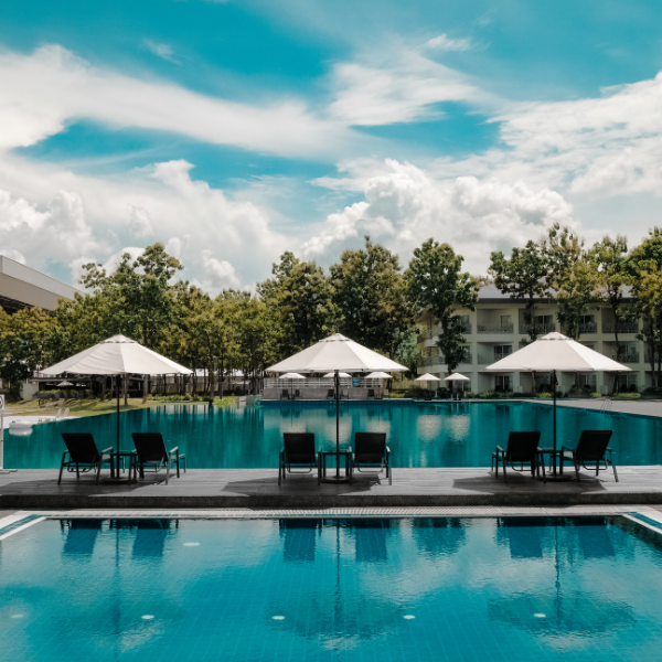 Swimming pool with lounge chairs, umbrellas, and surrounding trees under a partly cloudy sky.