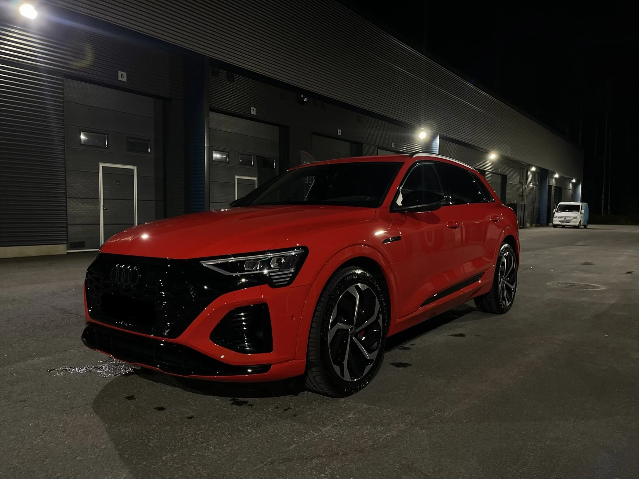 Punainen juuri putsattu ja fiksattu automalli Audi on parkkipaikalla yöllä, taustalla metalliseinän seinät ja vartinvalot.