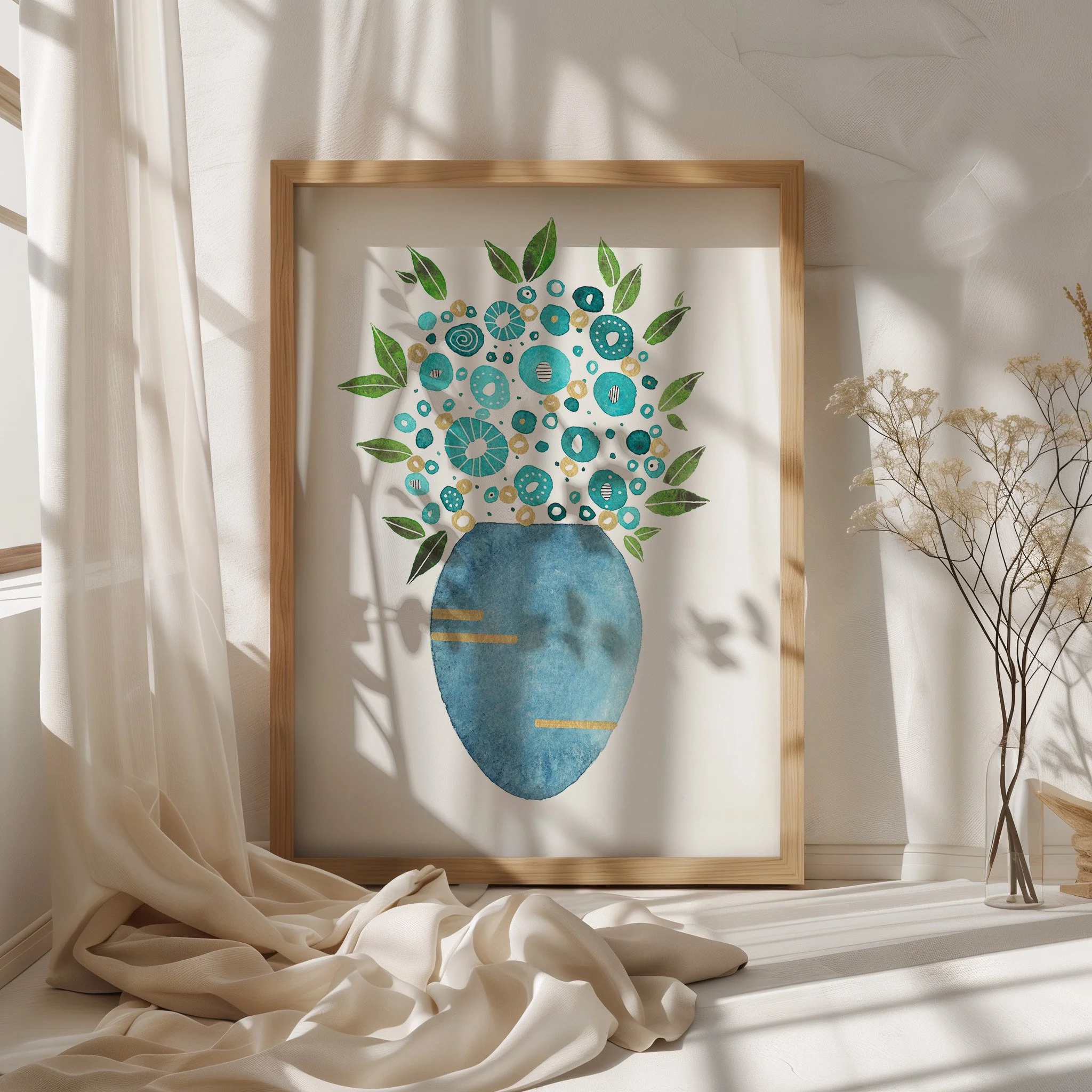 A framed abstract art piece with green leaves and blue circular patterns on a white background, leaning against a white wall, with sheer white curtains and dried plant accents nearby.