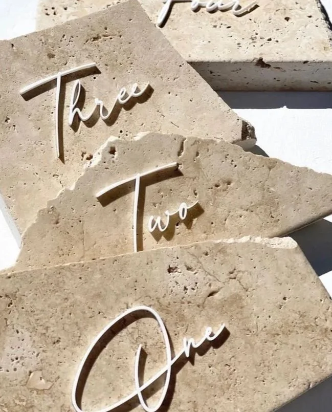 Three stone plaques with white cursive text reading 'One', 'Two', and 'Three', arranged in a staggered pattern on a white surface.