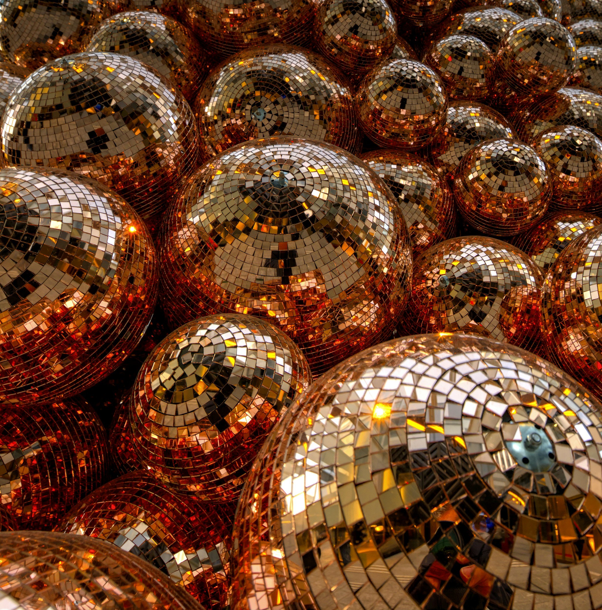 A close-up view of multiple gold-colored disco balls covered in small square mirror tiles, reflecting light and surrounding colors.