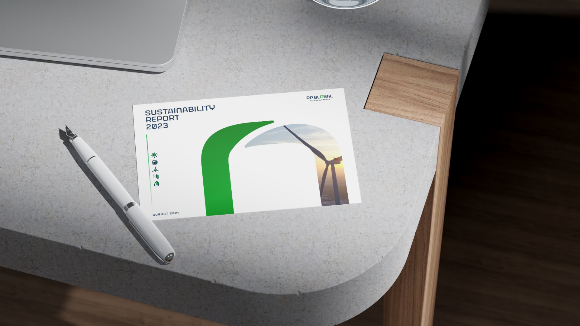 Sustainability report 2023 placed on a desk with a white pen nearby, a laptop at the upper left, and a small wooden block on the right; the report cover features a wind turbine and green graphics.