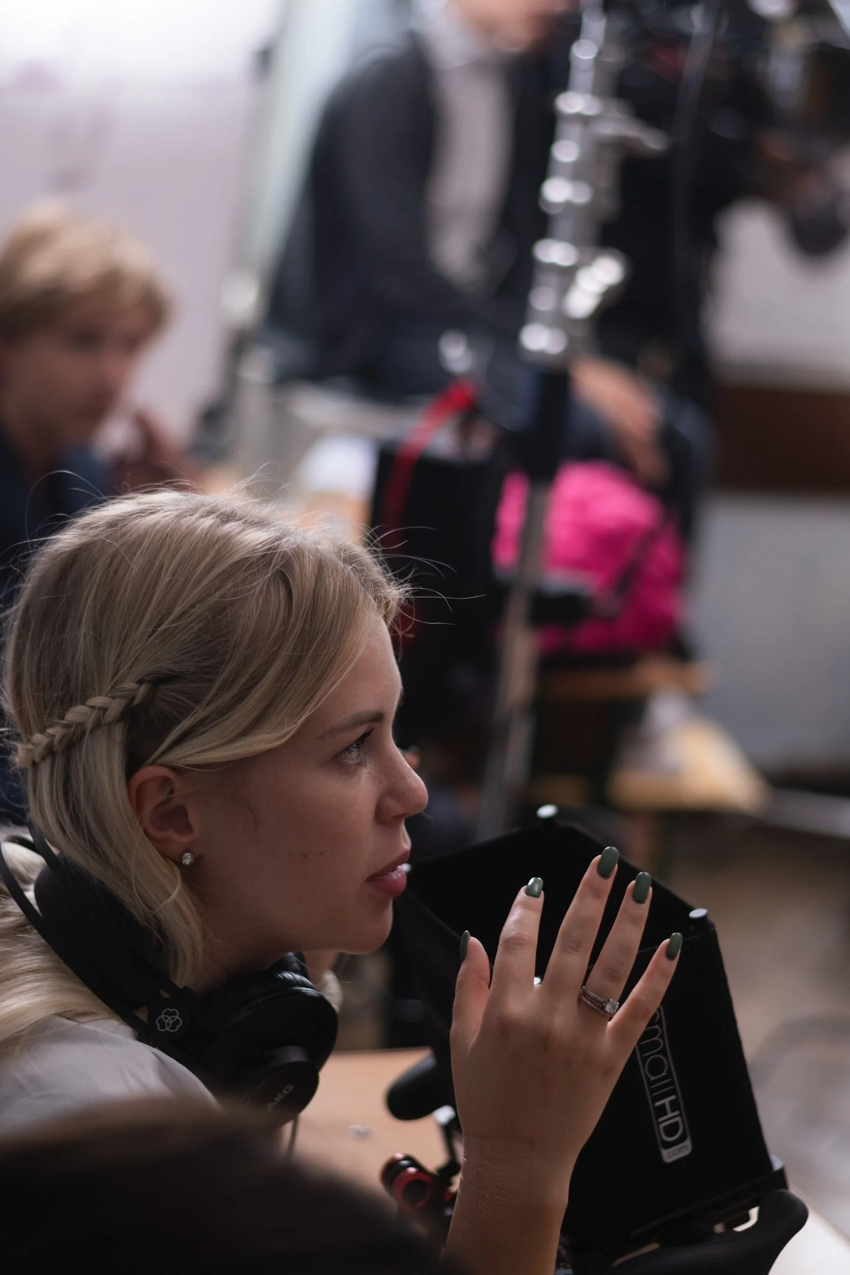 A woman with blonde hair and earrings, wearing headphones around her neck, is looking at her phone.