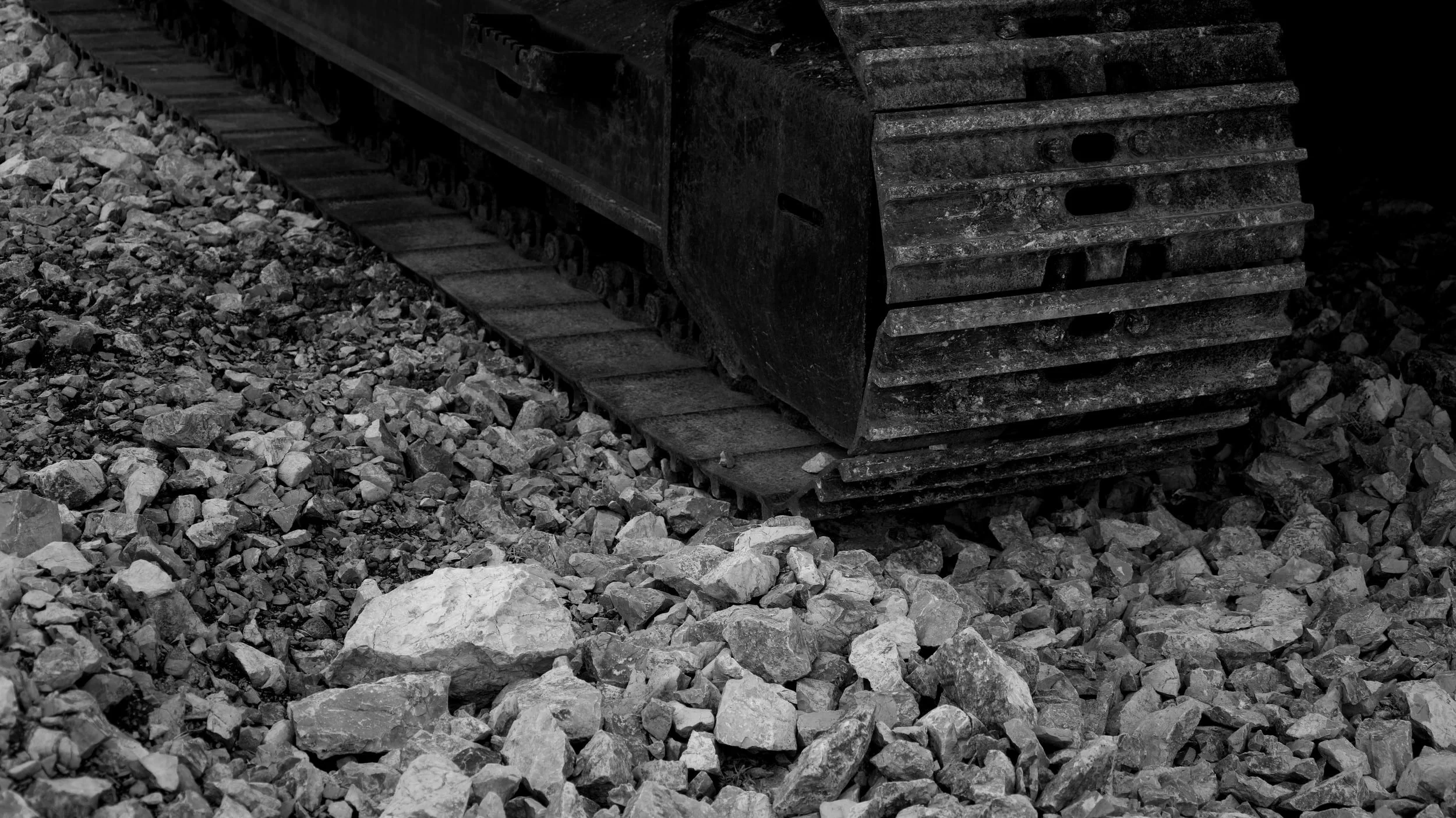 Close-up of a large bulldozer track on rocky terrain, black and white photograph.