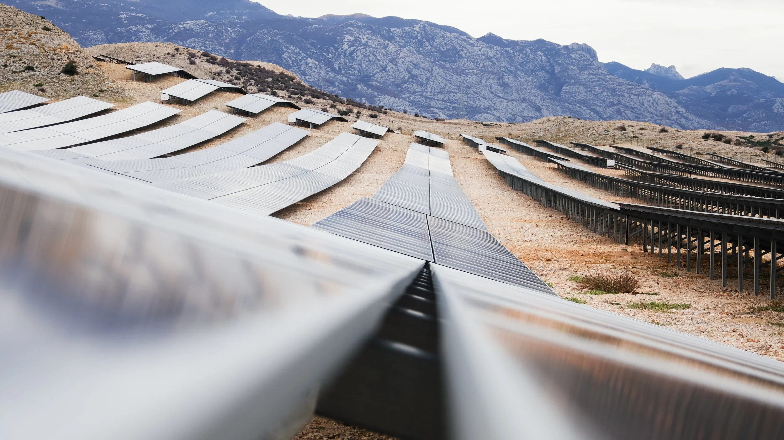 Multiple solar panels installed on a mountain slope, with mountains in the background.