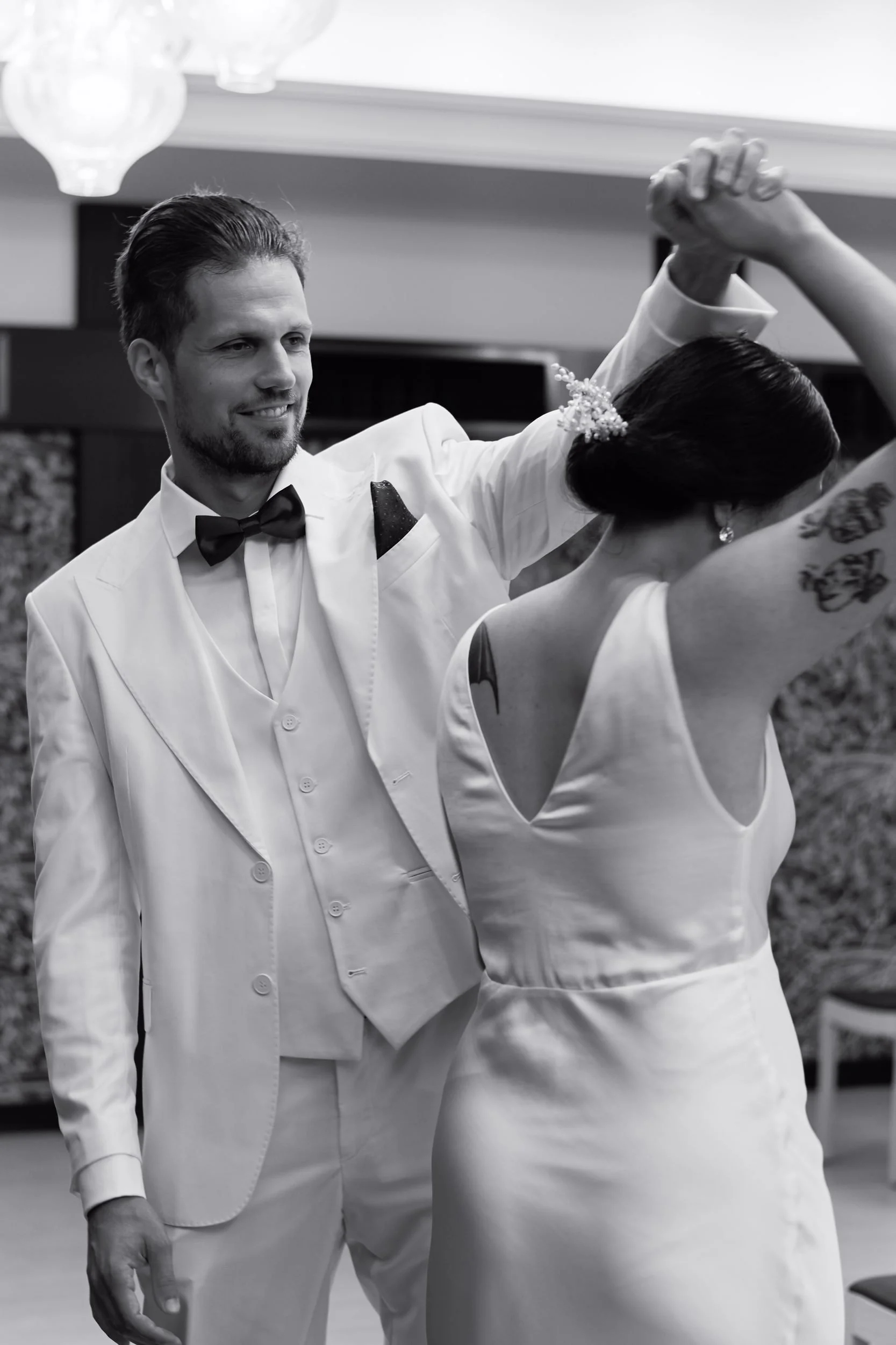 A man in a tuxedo holding hands with a woman in a wedding dress during a dance at a wedding reception.