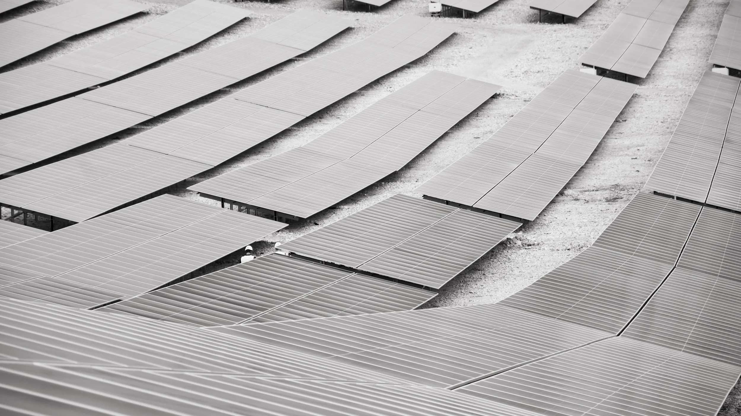 Multiple solar panels installed on the ground in a solar farm, arranged in rows with spaces in between.