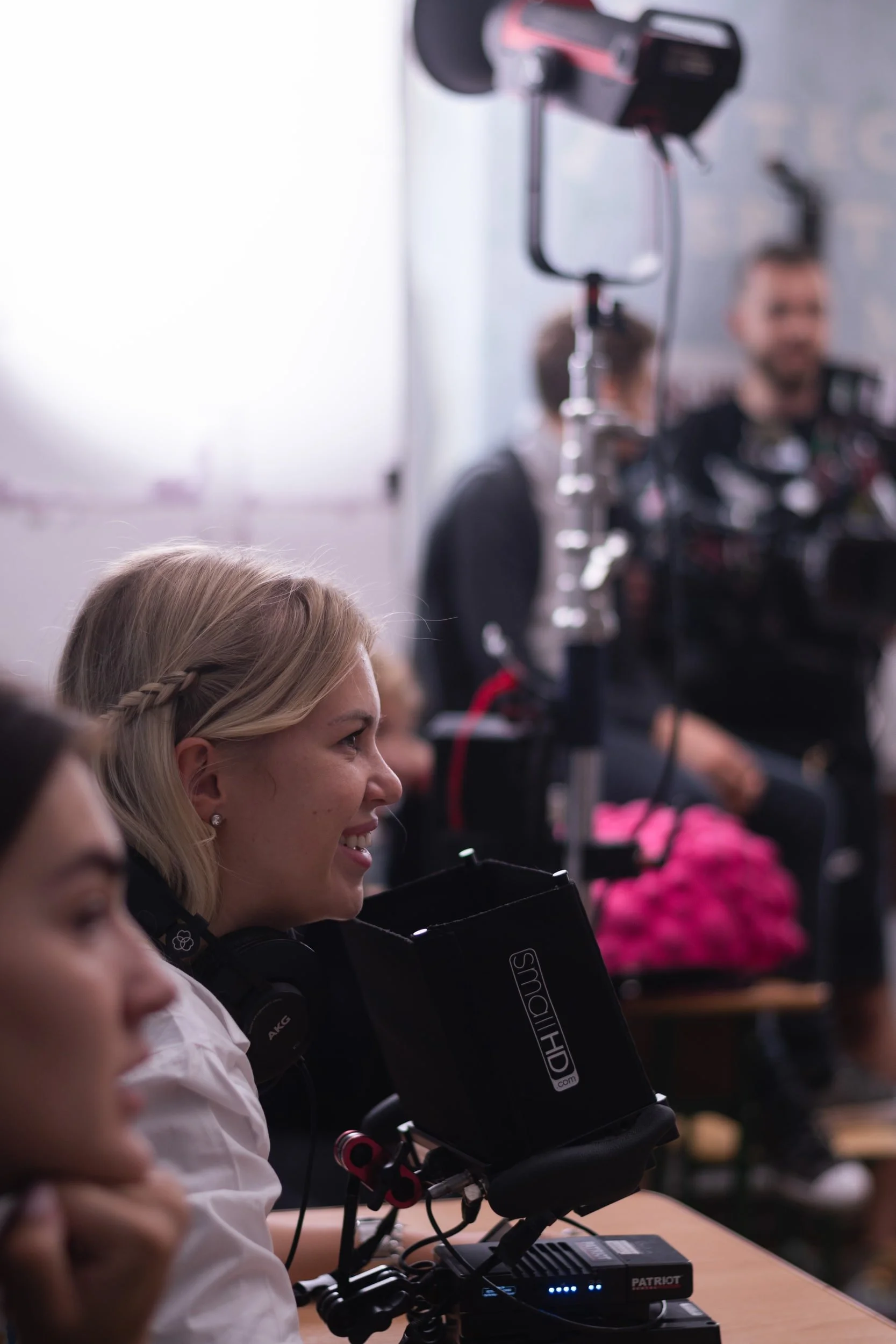 A group of students sitting in a classroom, wearing headphones, and looking at a computer monitor, with a teacher or instructor in the background.