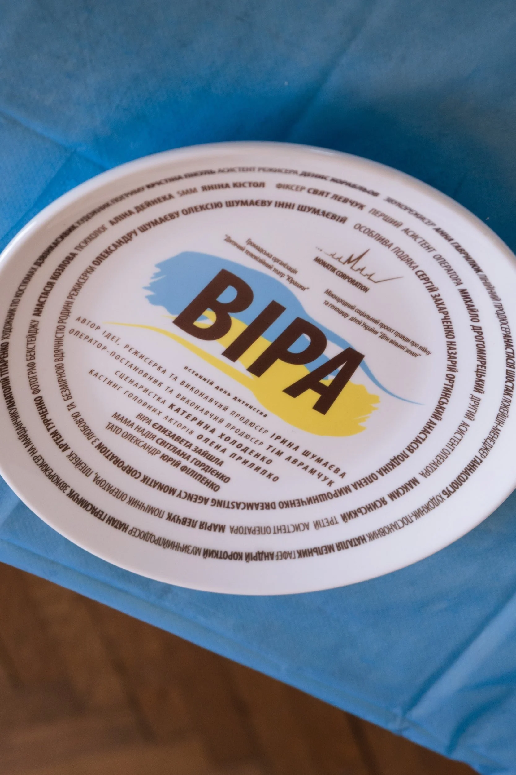 Close-up of a white cup with a colorful logo and Ukrainian text, placed on a blue surface.