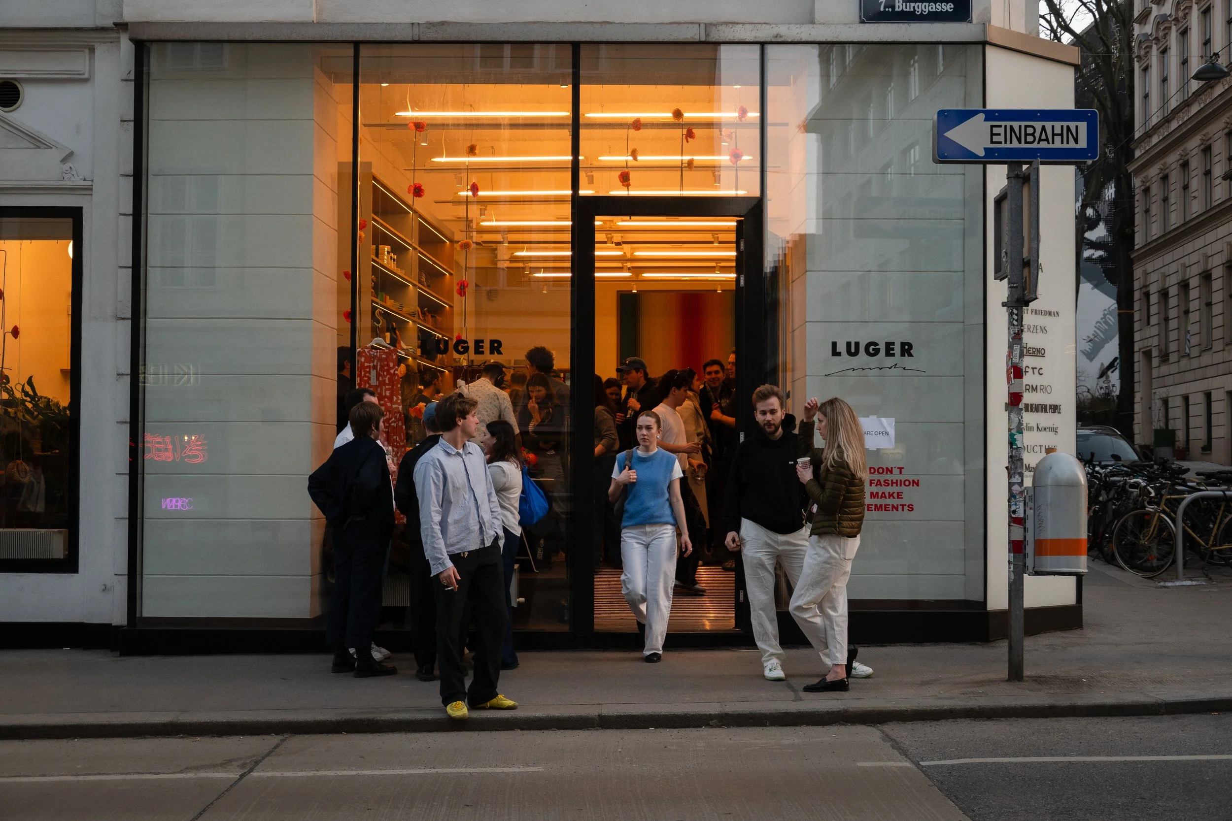 People standing and walking outside a modern store with large glass windows on an urban street.