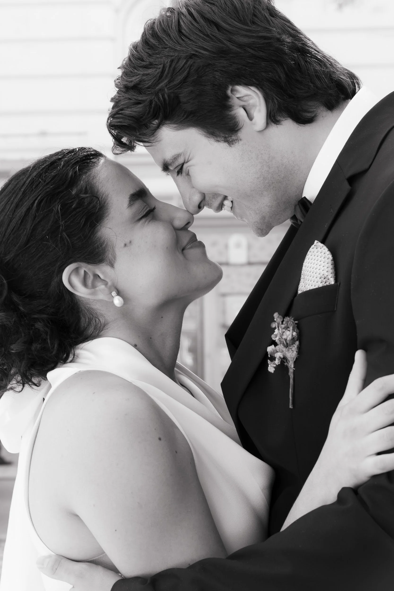 A black and white photo of a couple close together, their foreheads touching, smiling with eyes closed, dressed formally, suggesting an intimate or romantic moment.