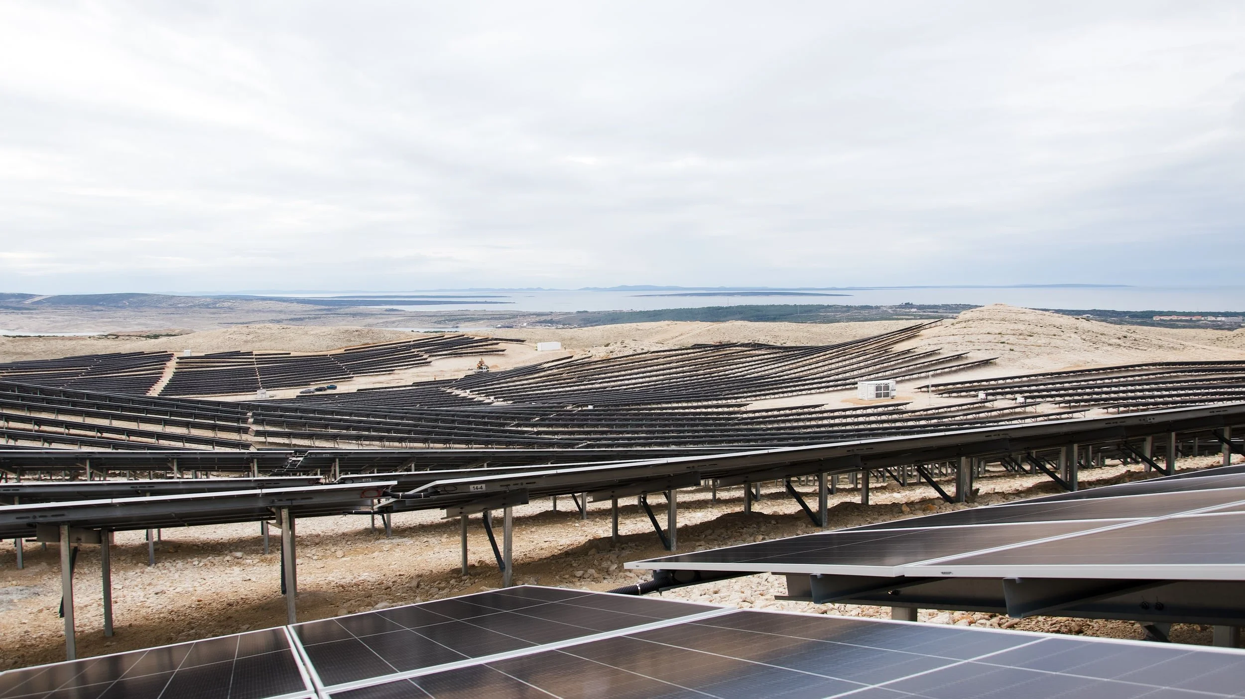 Solar panels installed on a landscape with a body of water and cloudy sky in the background.