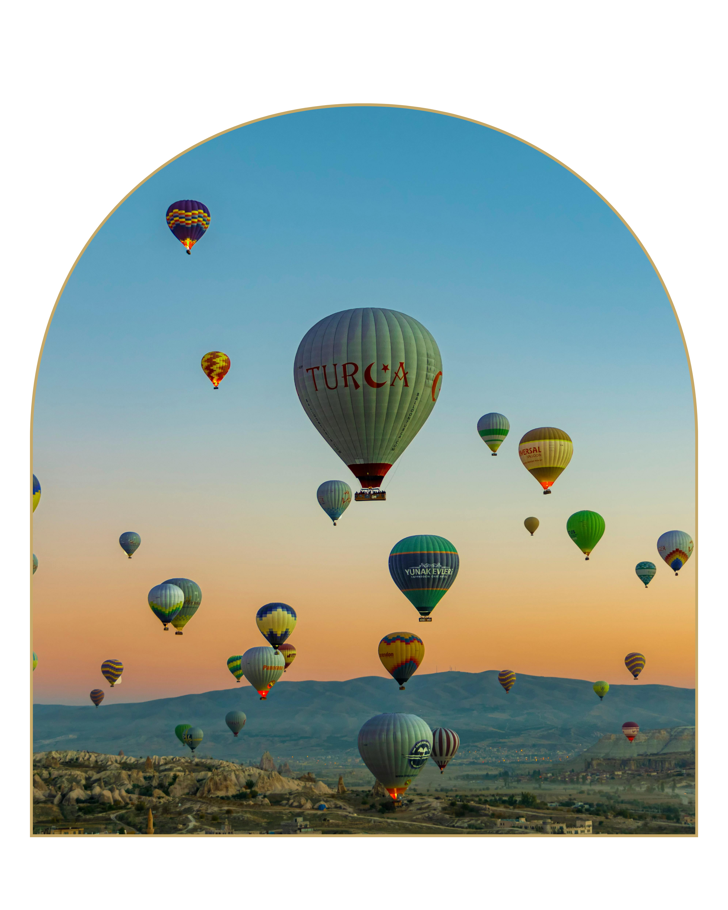 Multiple hot air balloons floating over a desert landscape during sunrise or sunset, with a range of mountains in the background.