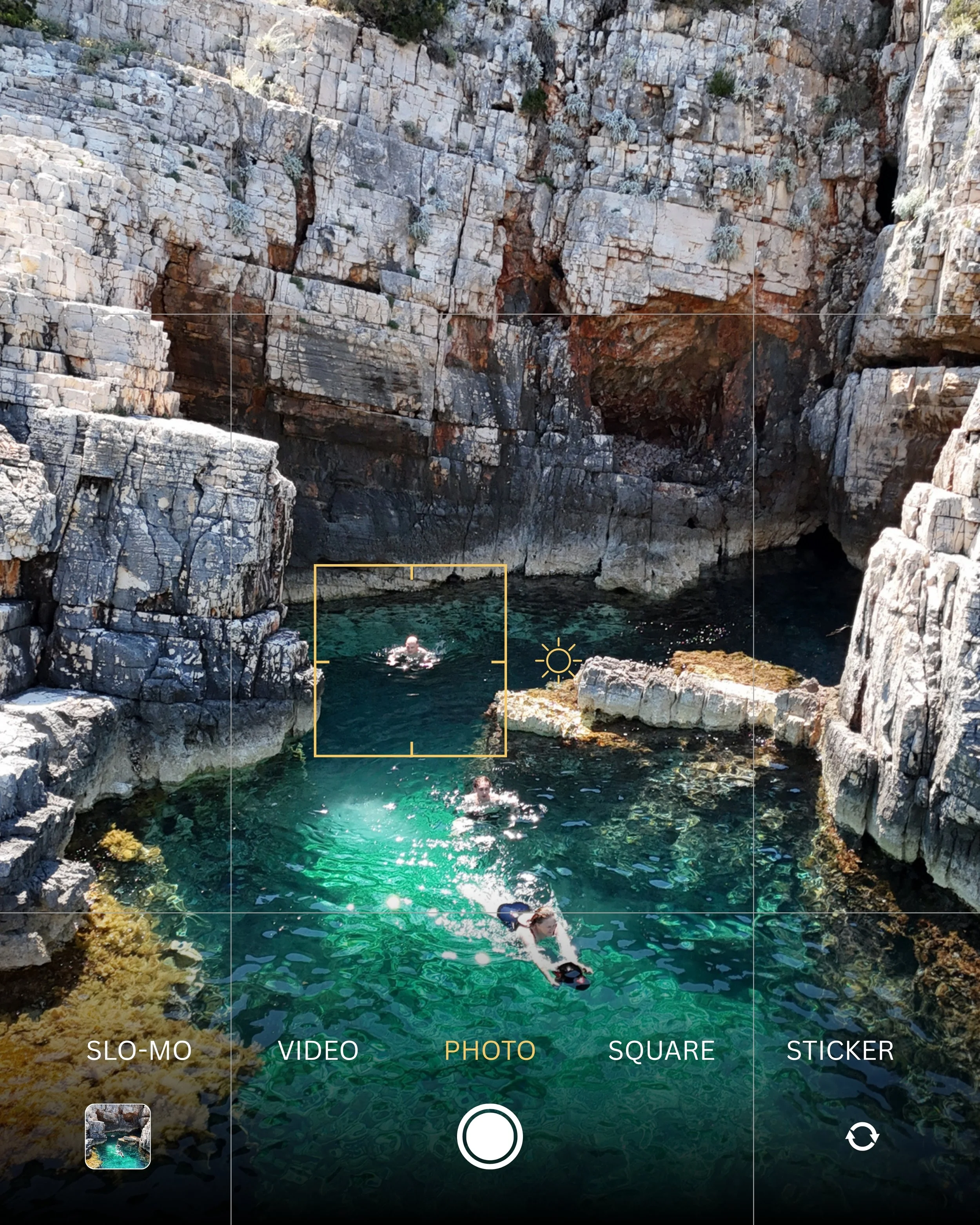 A person swimming in a clear, rocky waterhole surrounded by rugged cliffs and sparse vegetation.