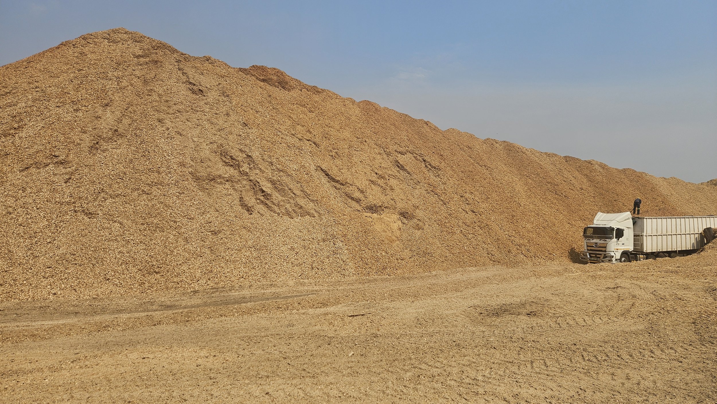 A large dirt pile with a white truck parked nearby under a clear sky.