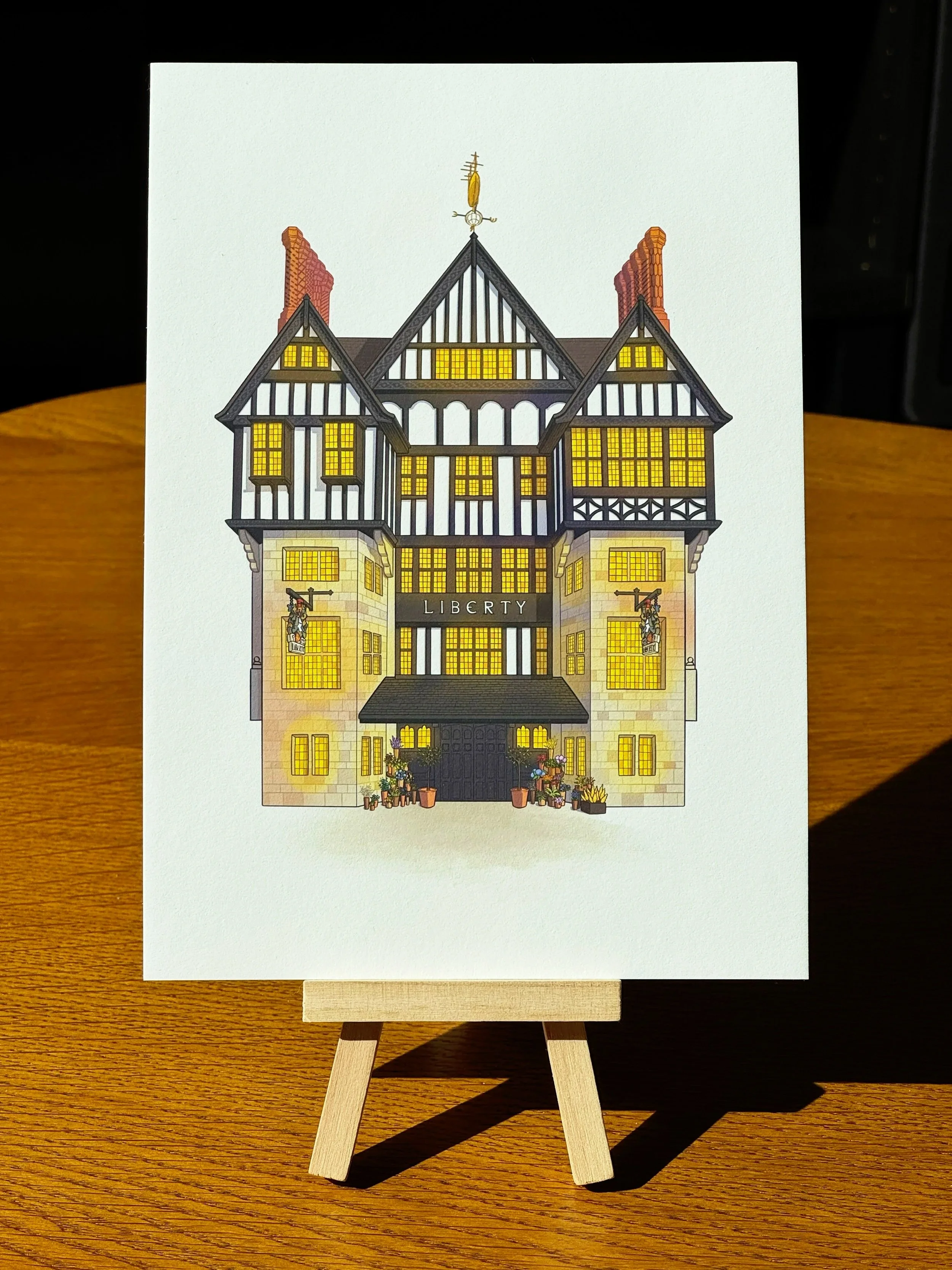 A miniature drawing of a traditional house with the word 'Liberty' on the front, displayed on a small easel on a wooden surface.