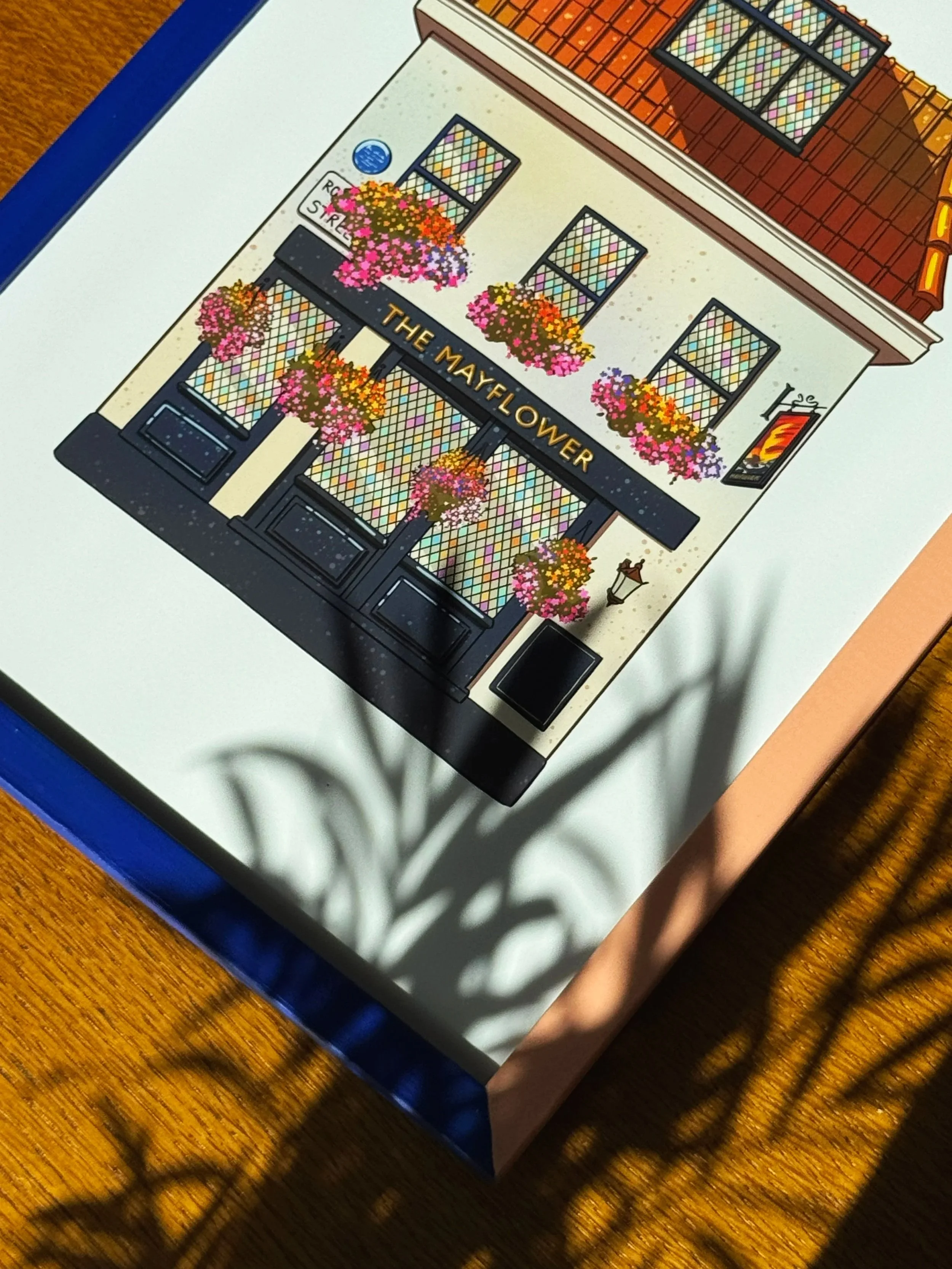Drawing of the exterior of a building called 'The Mayflower' with pink, orange, and yellow flowers in baskets and a streetlamp in front.